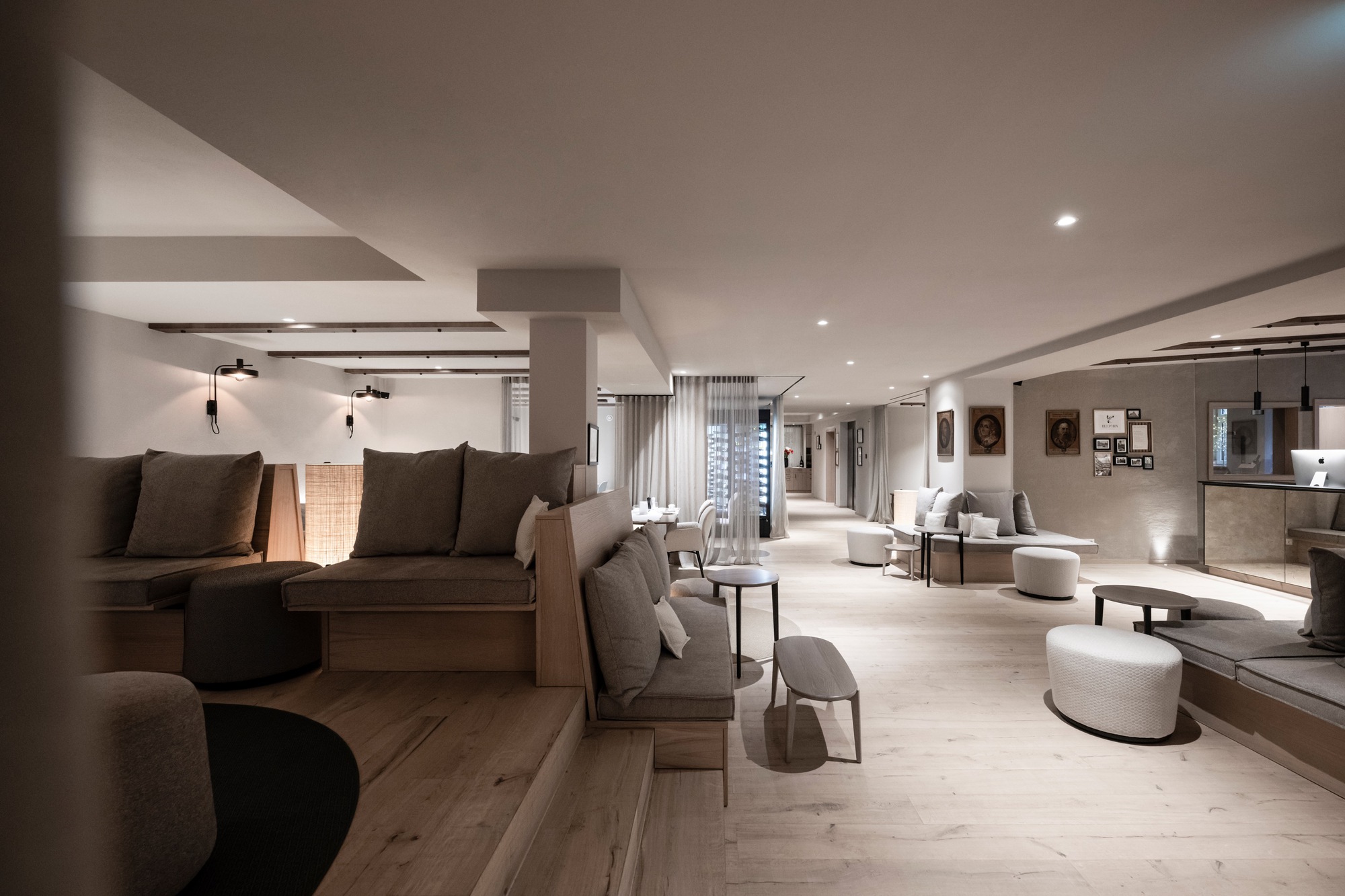 Open lounge area with upholstered seating clusters and wide timber floor under recessed ceiling lighting