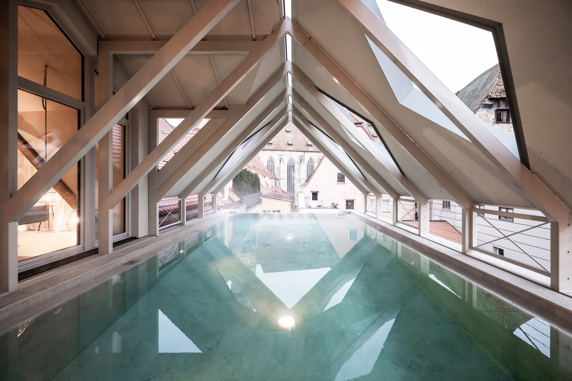 Long view of the rooftop pool framed by diagonal timber beams and continuous slope glazing