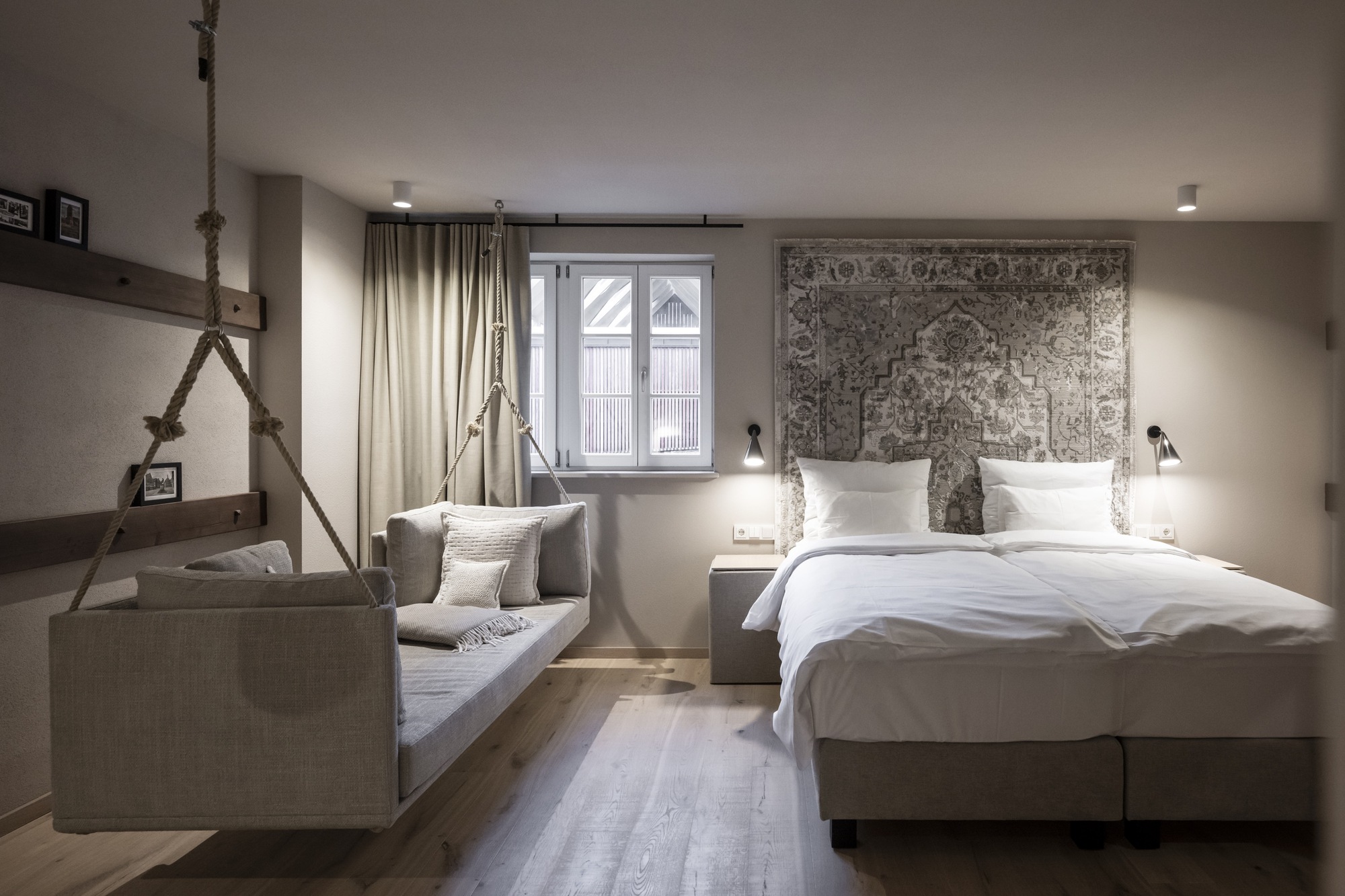 Guest room with rope-suspended bench seating and patterned wall hanging behind the bed