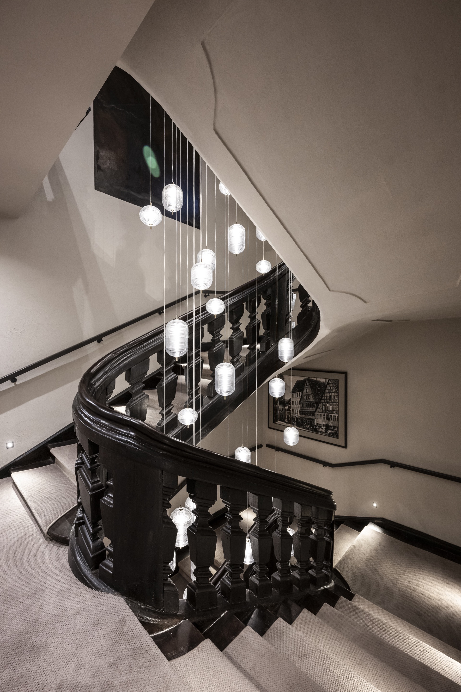 Curved staircase with black wood balustrade and cascading globe pendant lights in the stairwell
