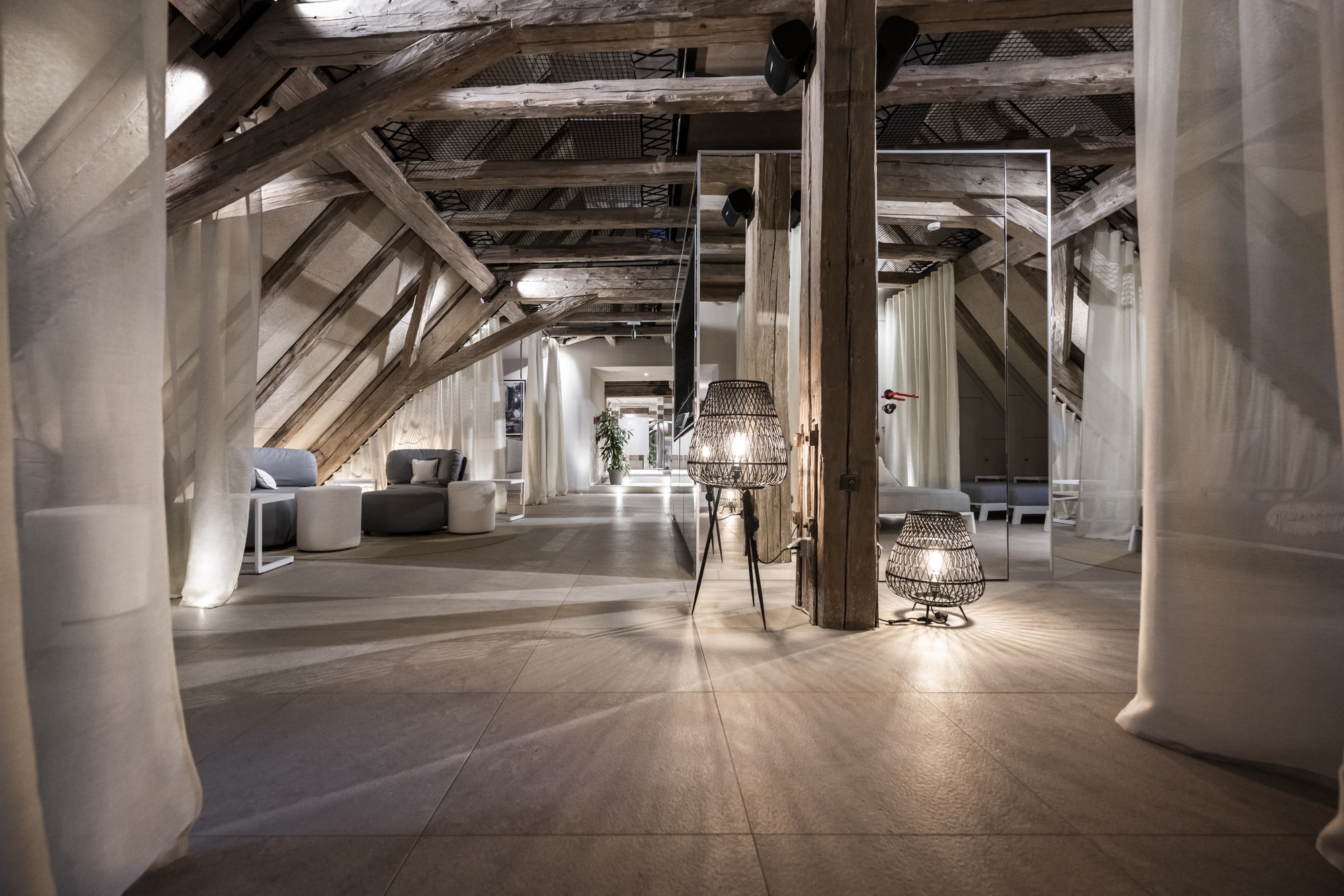Attic interior with exposed timber trusses, concrete columns, and wicker pendant lights along a polished floor