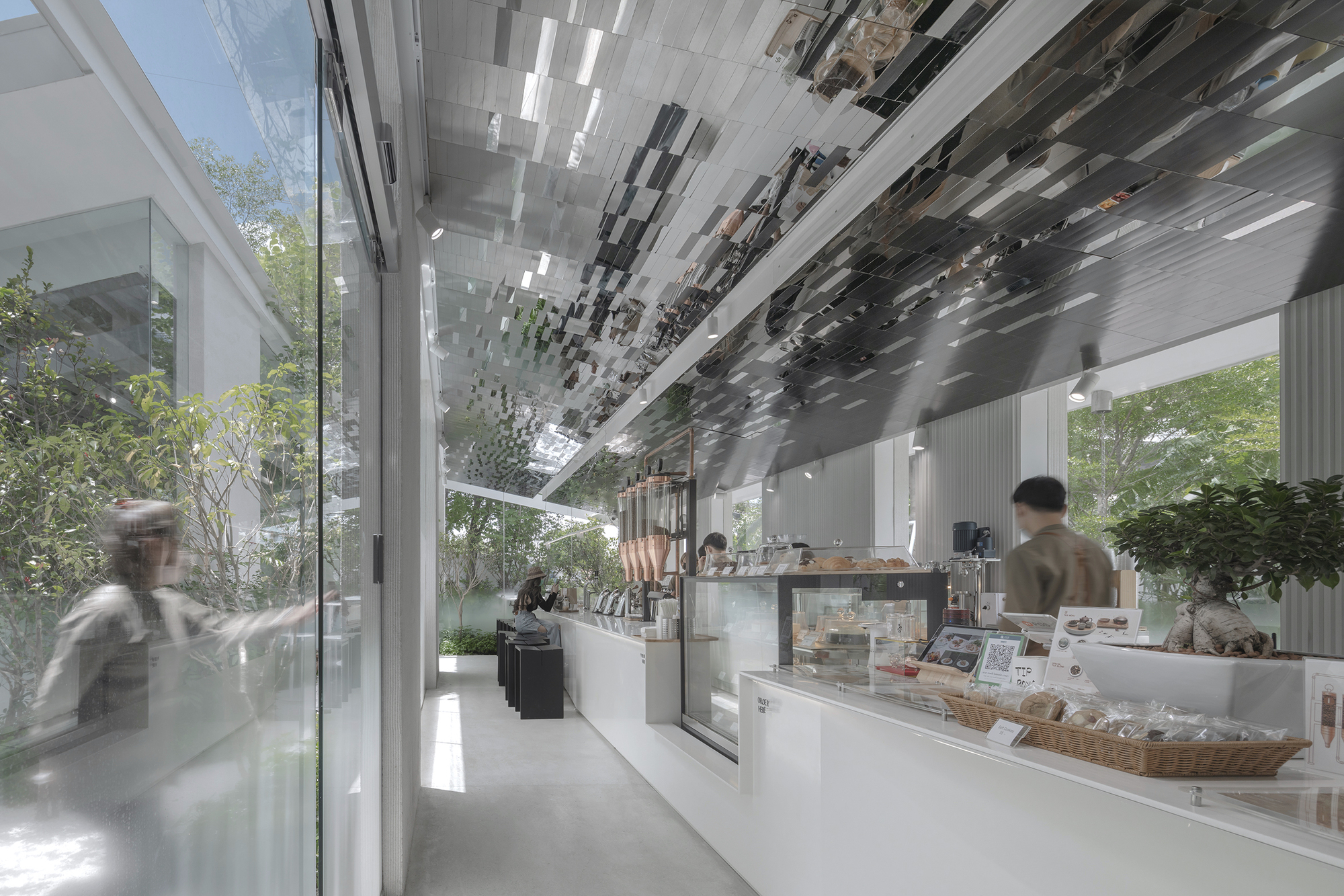Service counter with bakery display cases under a patterned ceiling with blurred figures walking past