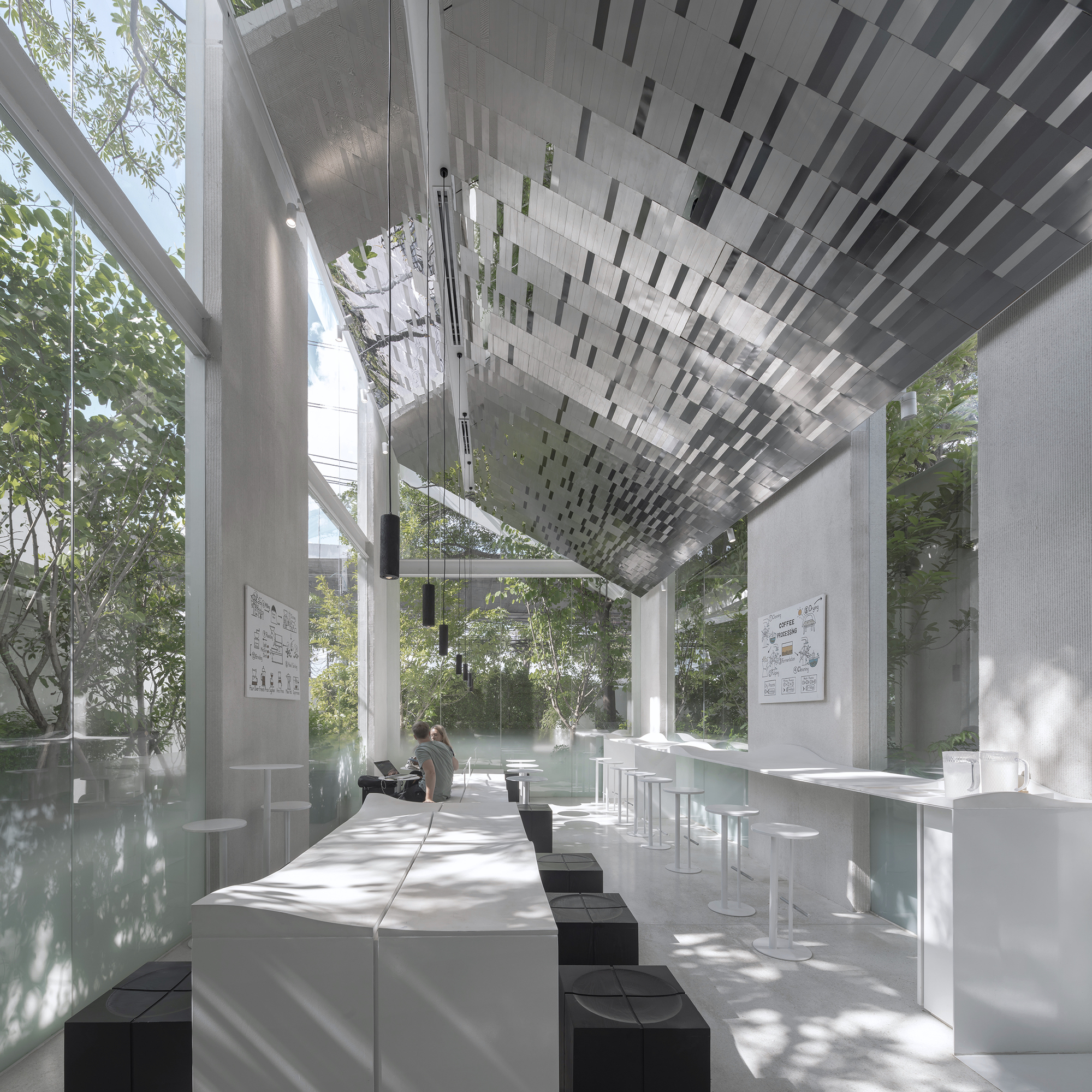 Interior seating area with white tables and black stools under geometric monochrome ceiling panels