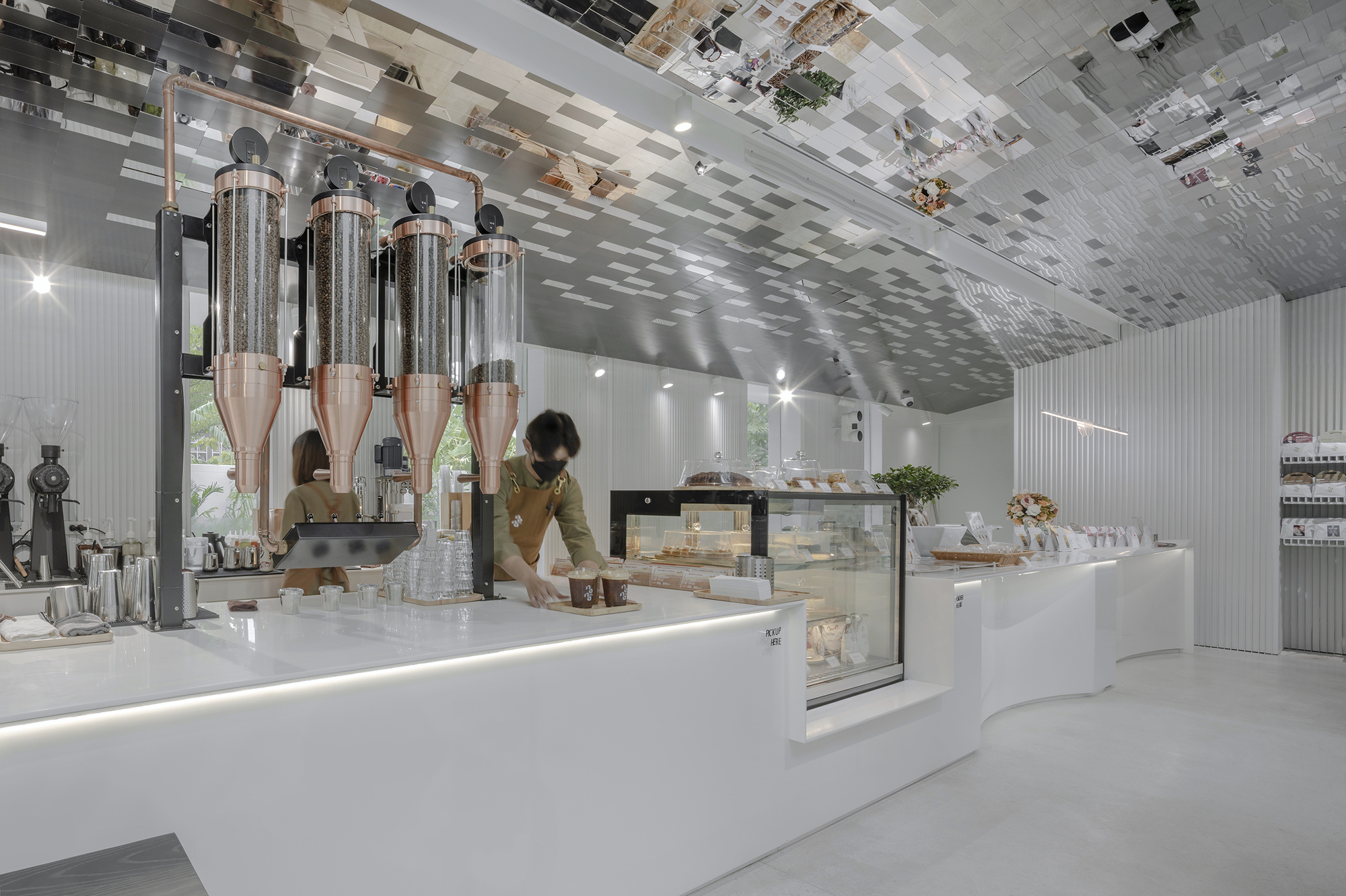 Coffee service counter with chrome dispensers and a barista arranging cups beneath reflective ceiling treatment