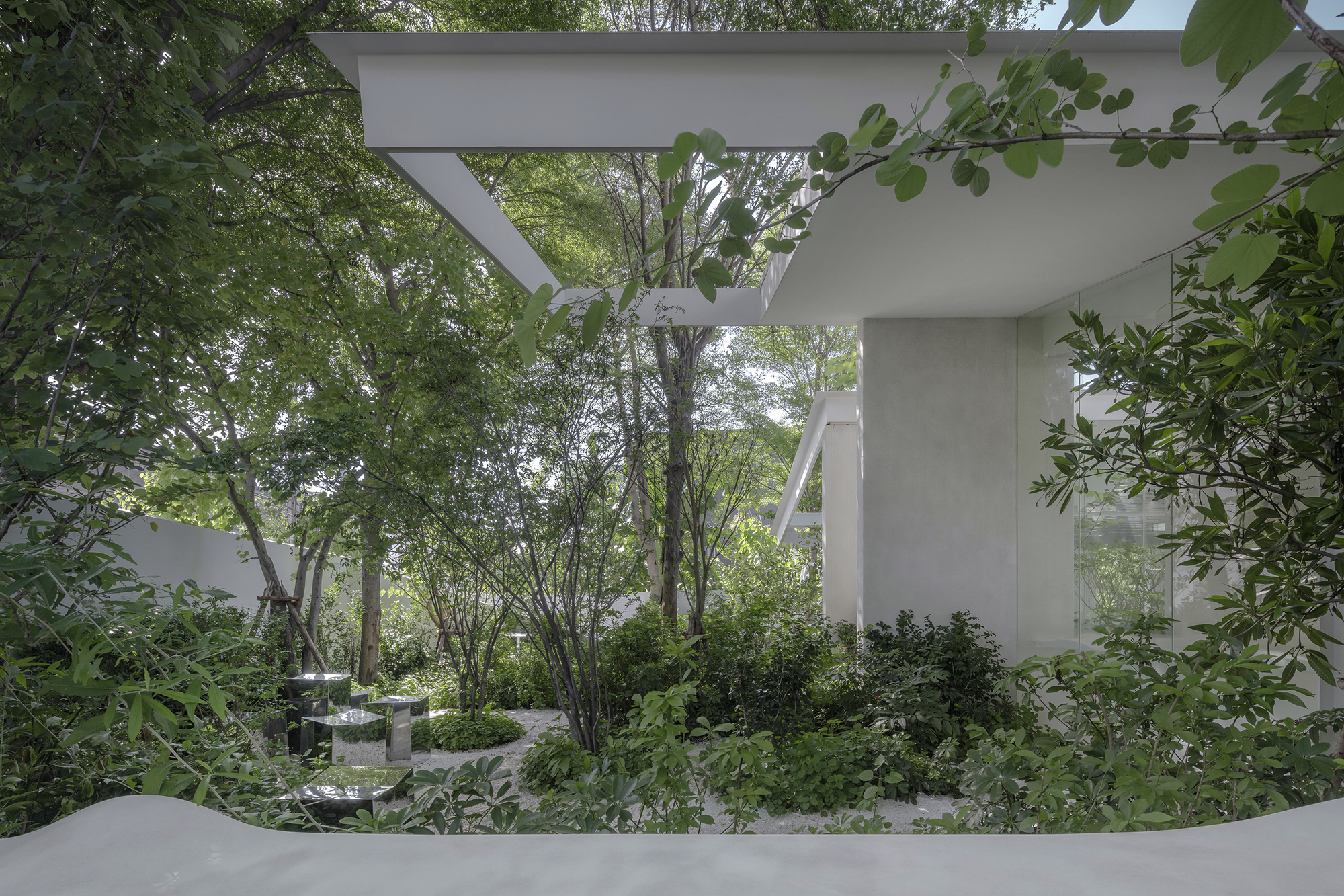 White concrete canopy and columns framing a planted courtyard with mature trees and dense foliage