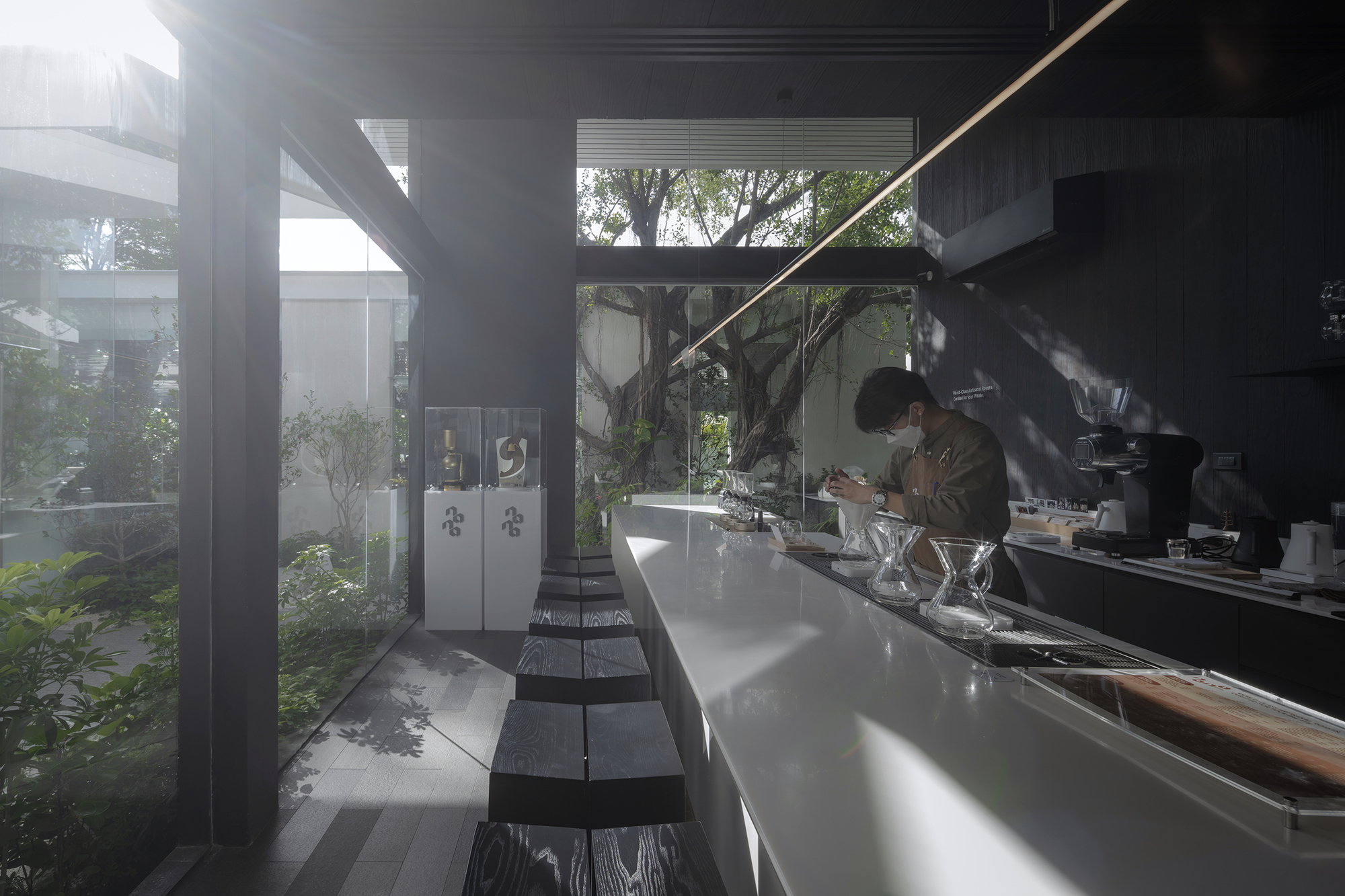 Interior counter bar with white surface and black stools overlooking a planted courtyard with mature tree