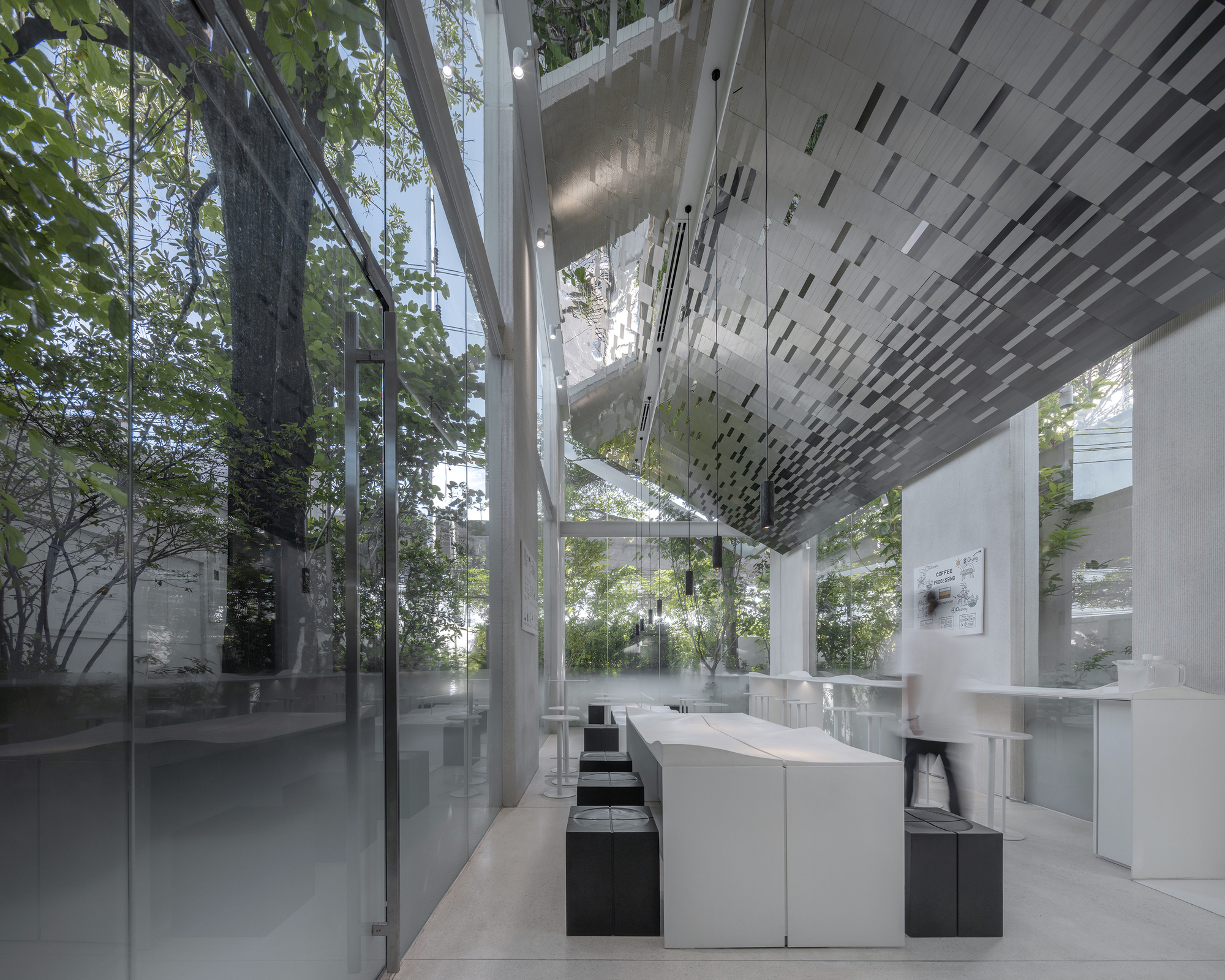 White service counter beneath perforated ceiling panel with full-height glazing framing trees outside