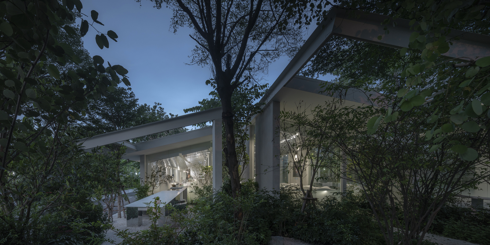 Exterior view of concrete frame structure nestled among mature trees and foliage at twilight