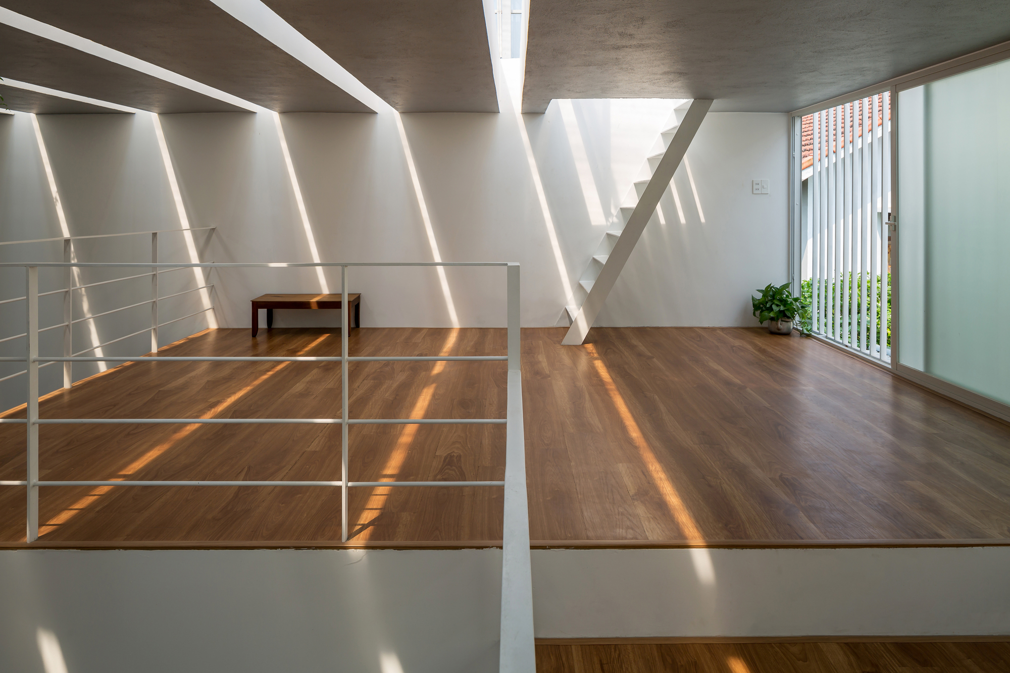 Wood-floored mezzanine with white metal railing and diagonal light stripes from overhead skylights