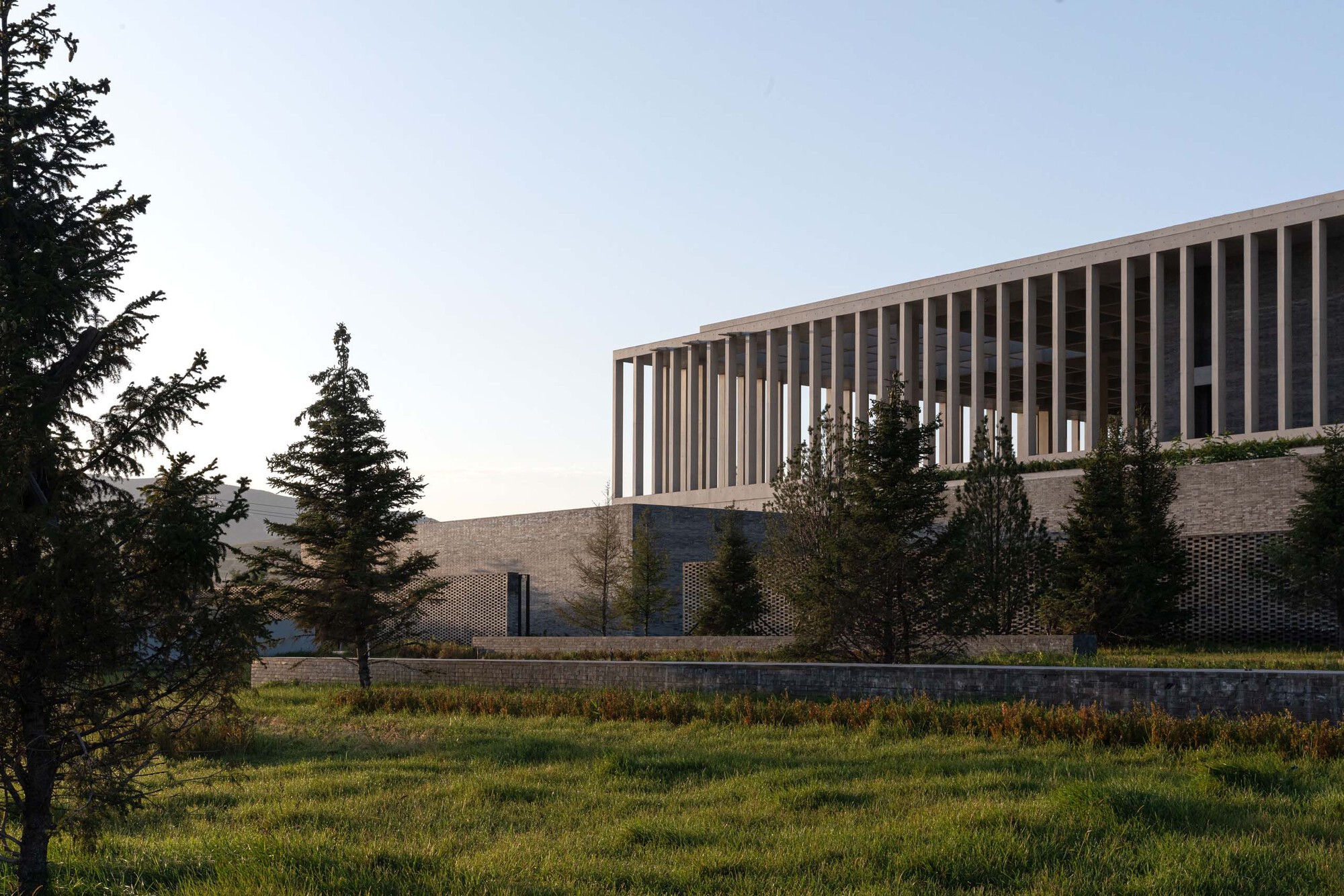 Stone base with patterned brickwork topped by a vertical louver screen among evergreen trees