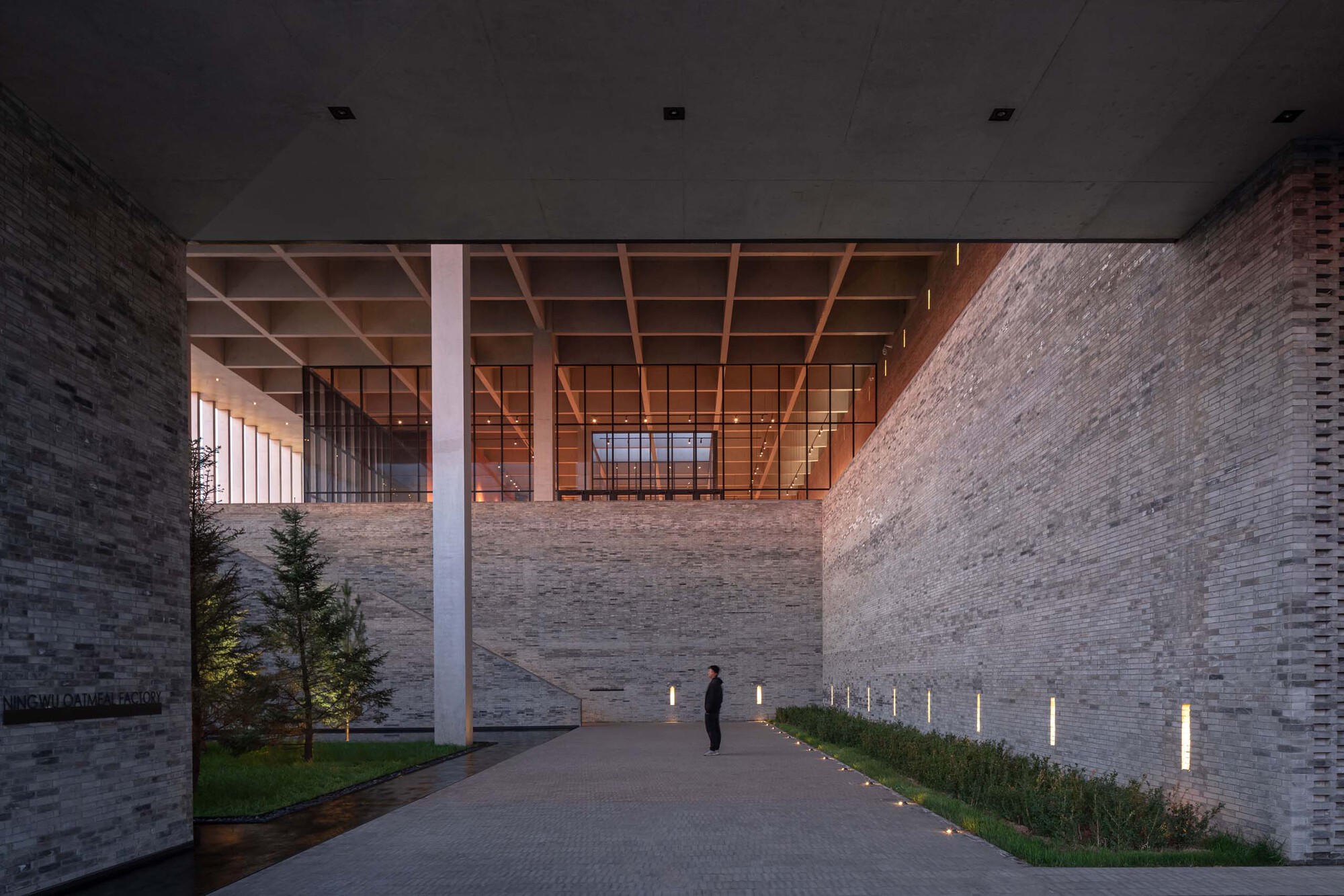 Covered entrance passage with timber coffered ceiling and a figure walking between masonry walls at twilight