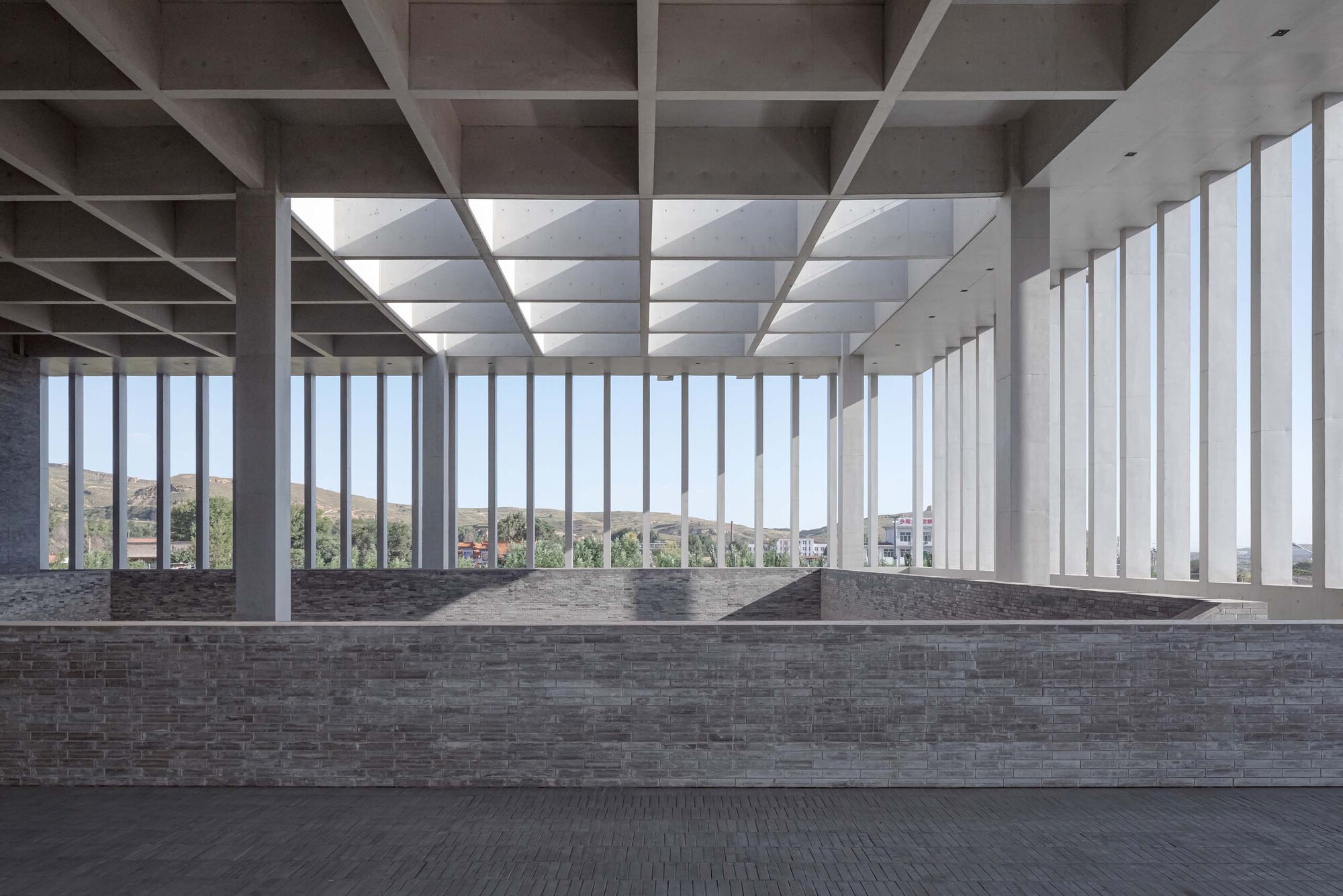 Interior hall with coffered concrete ceiling and vertical fin windows overlooking distant hills