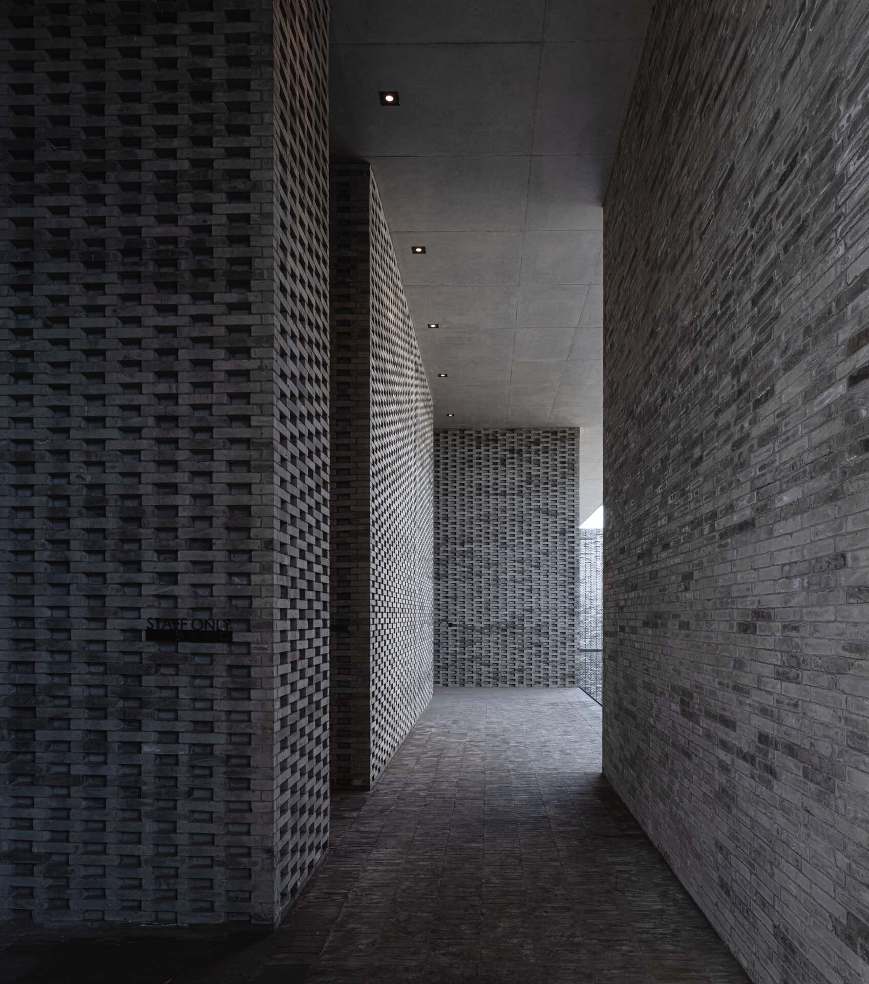 Narrow corridor with basketweave brick walls and recessed ceiling lights leading deeper into the space