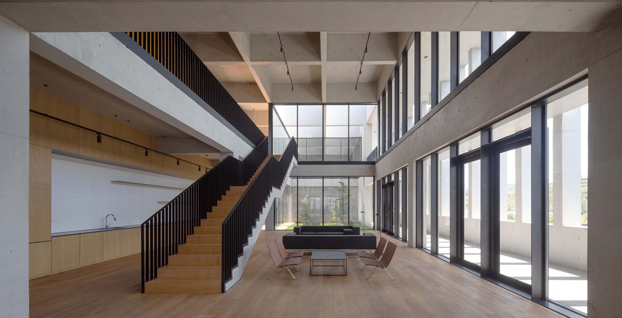 Double-height lobby with timber staircase, concrete coffered ceiling and floor-to-ceiling glazing overlooking trees