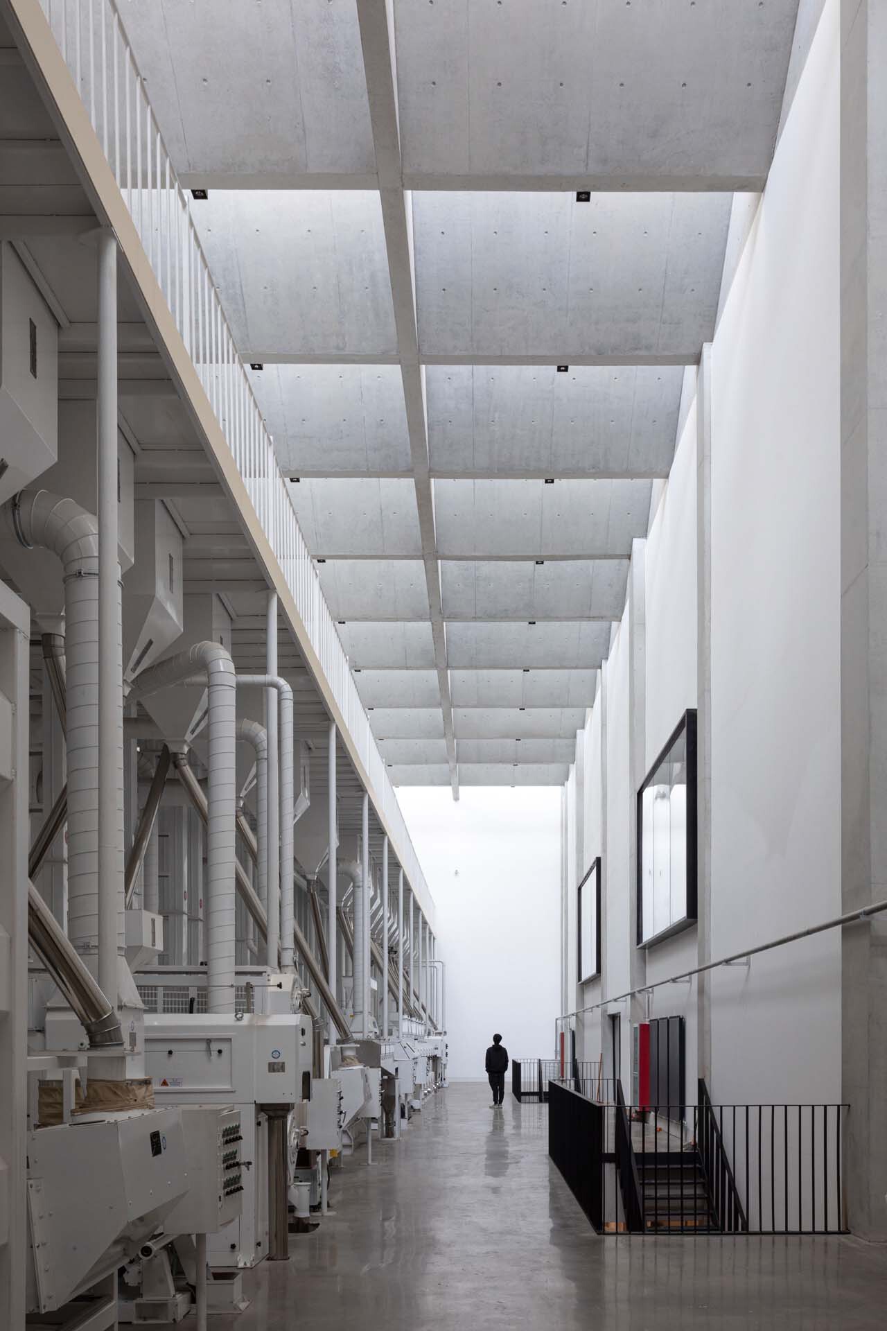 Industrial gallery with exposed white mechanical ducts along one wall and coffered concrete ceiling overhead