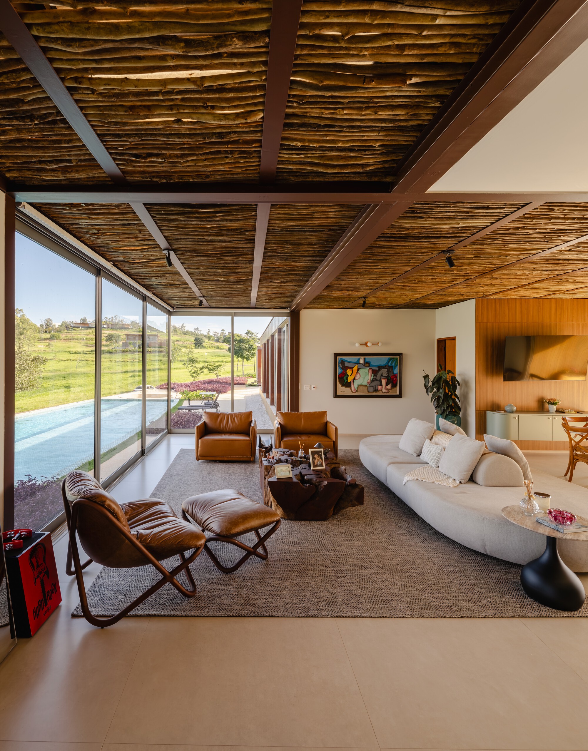 Living room with exposed timber-strip ceiling, floor-to-ceiling glazing and view to rolling landscape beyond pool terrace