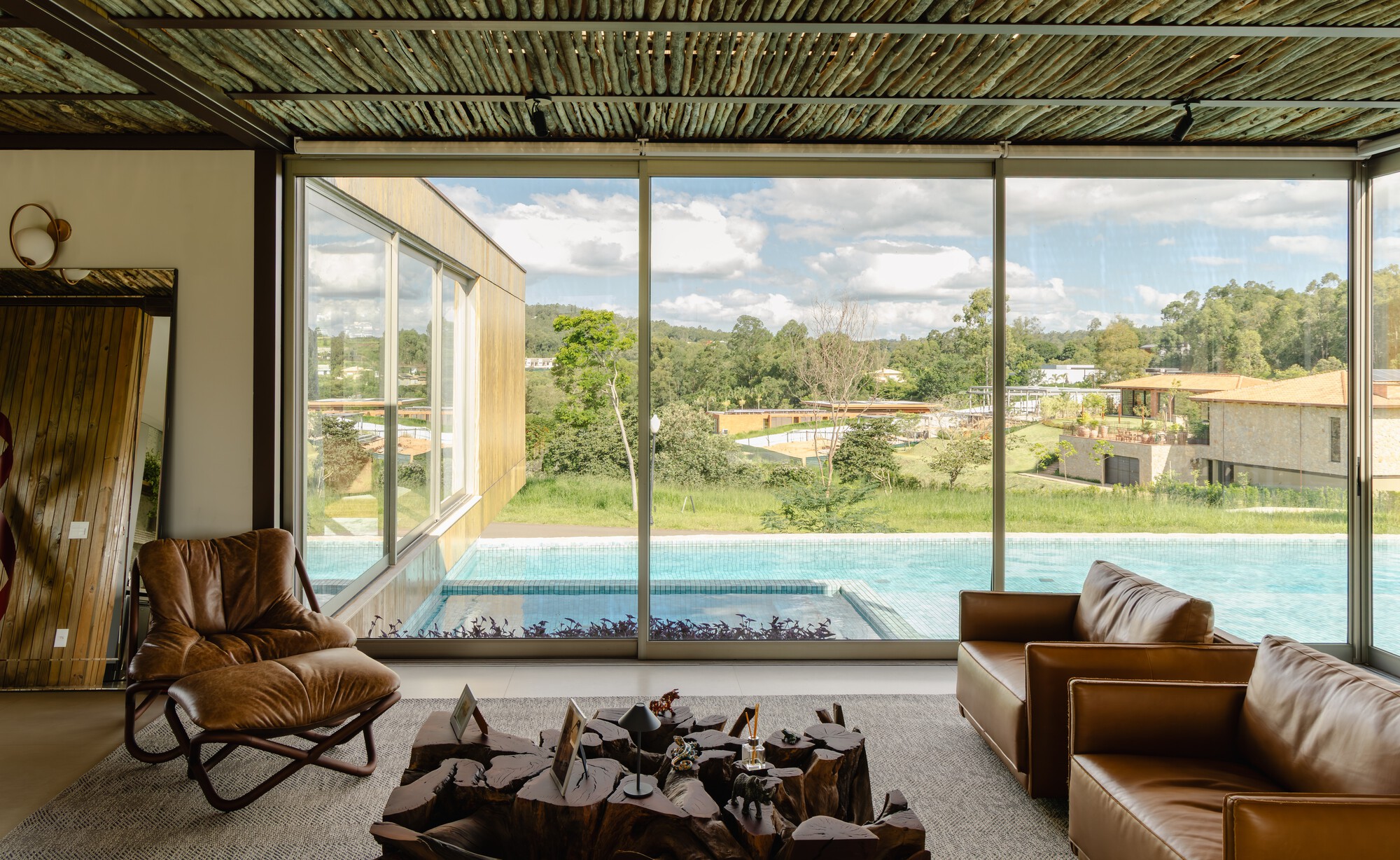 Interior view to swimming pool and landscape through floor-to-ceiling glass under slatted timber ceiling