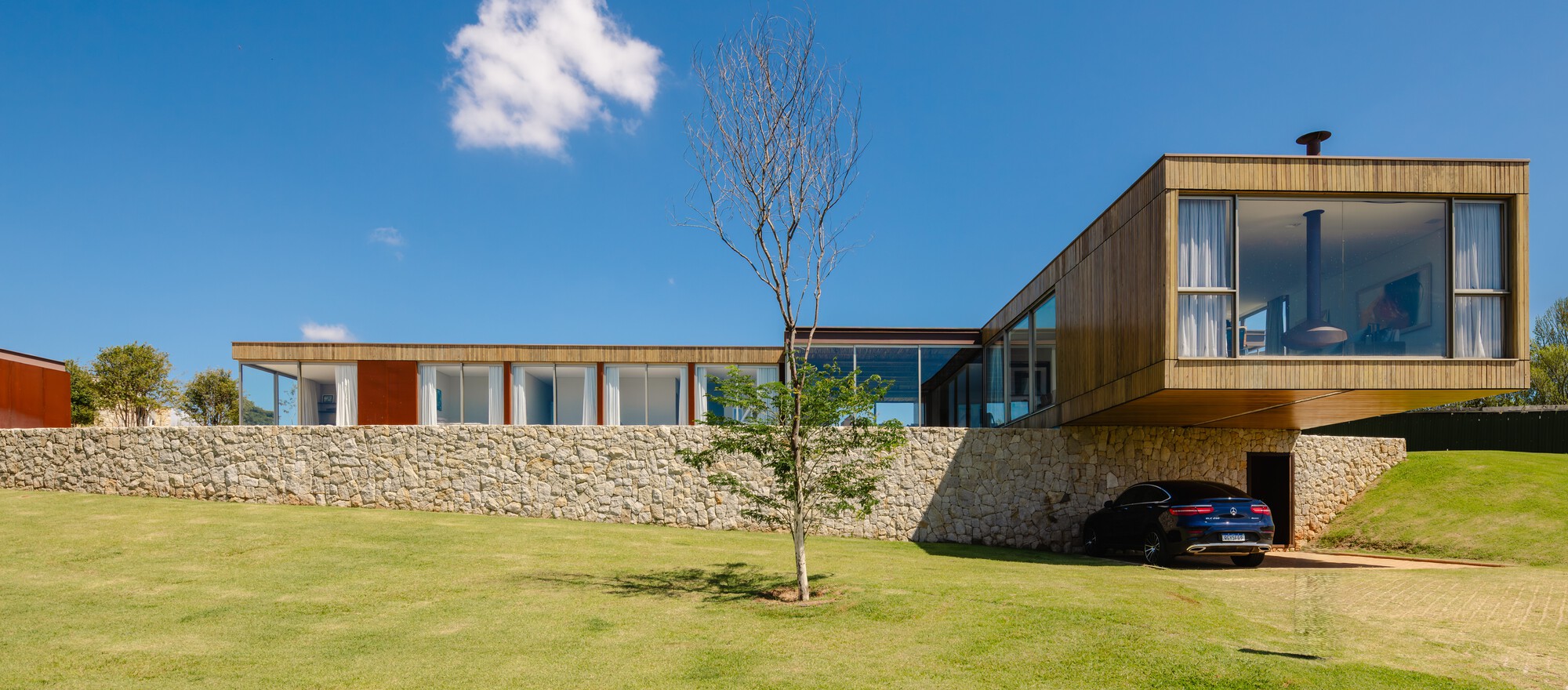 Horizontal facade with timber cladding and glass openings rising above a stone retaining wall