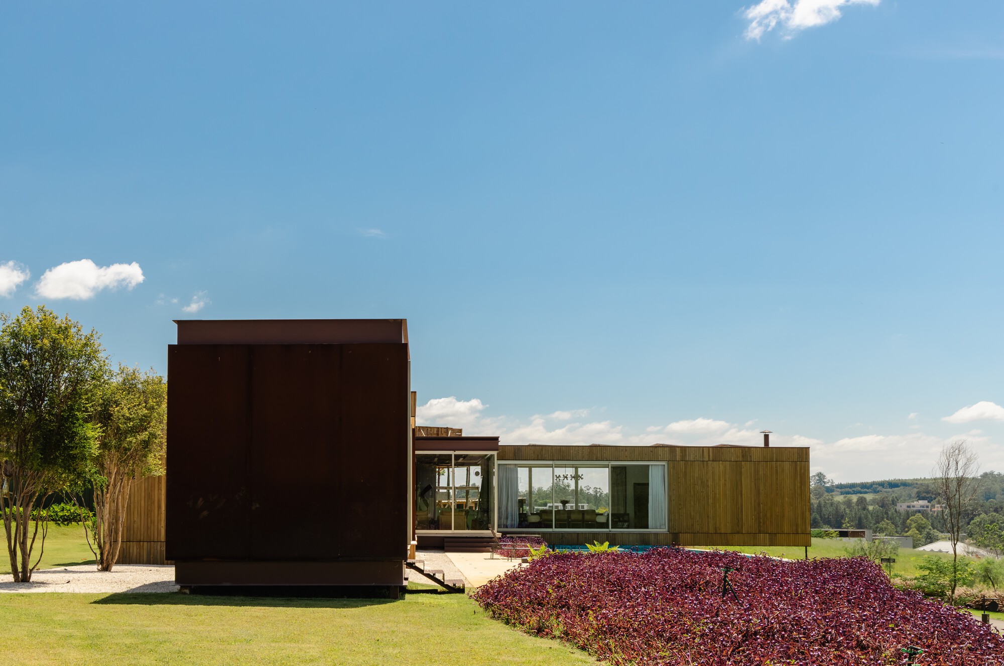 Garden elevation showing dark corten volume and horizontal timber wing with red foliage bed