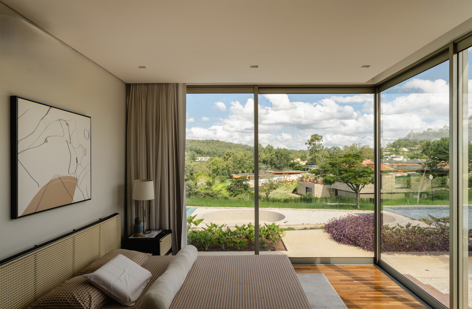 Bedroom with floor-to-ceiling glass doors opening to a garden with purple foliage and cloud-filled sky