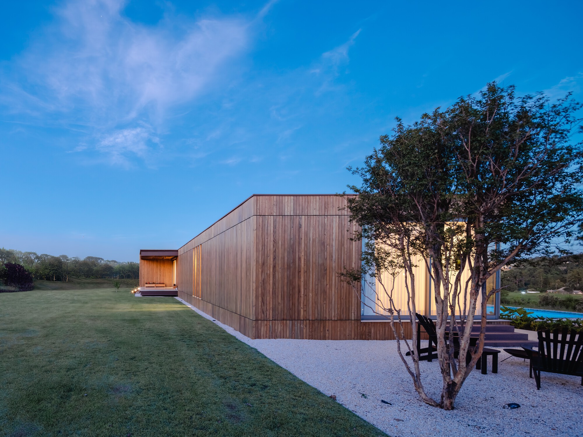 Vertical timber cladding along the facade with a tree in gravel beside the building