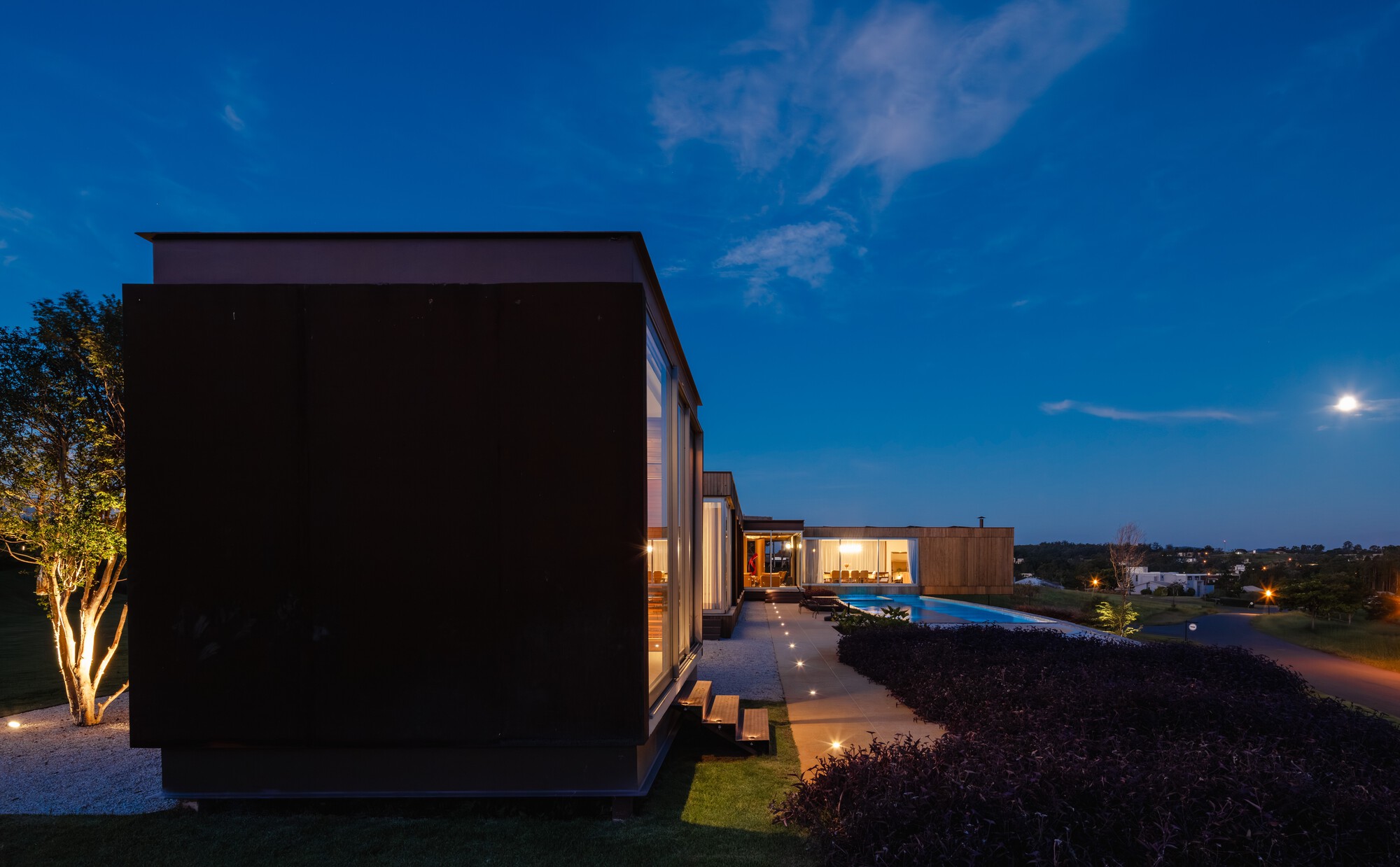 Dark geometric volumes arranged around a pool terrace at twilight under the moon