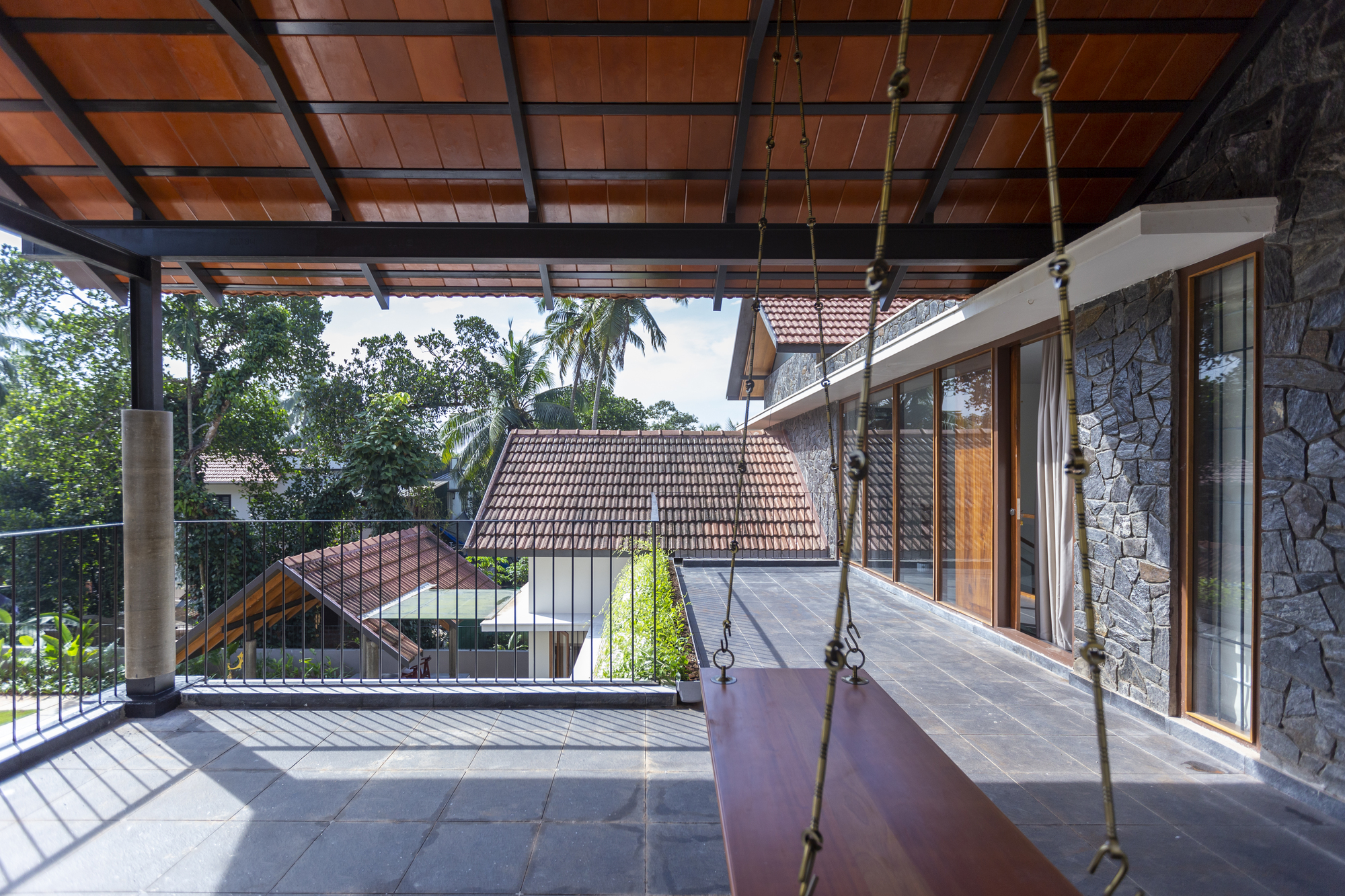 Covered terrace with timber ceiling grid, hanging swing, and view of tiled roofs beyond