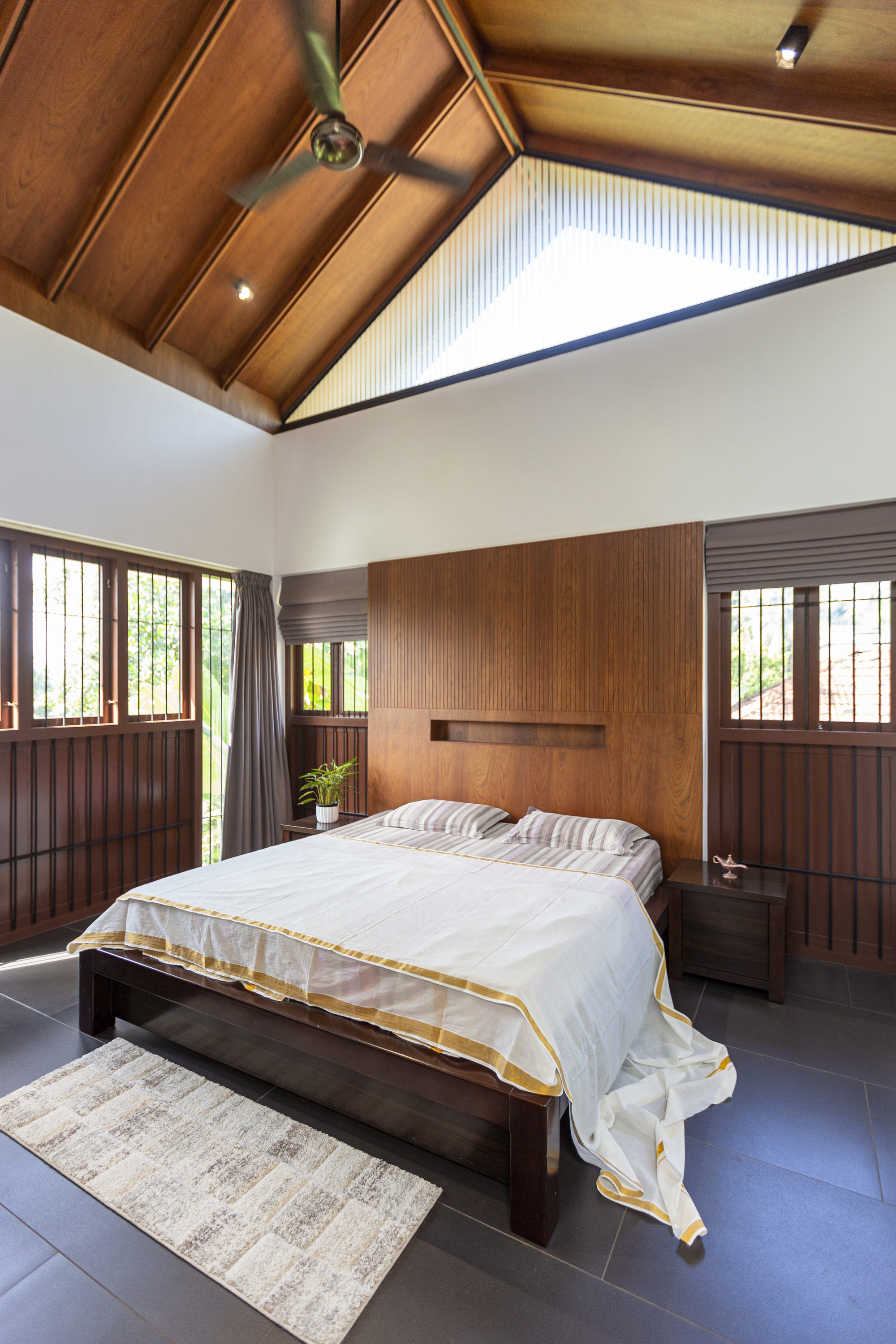 Bedroom with vaulted timber ceiling, wood-paneled walls, and symmetrical windows on either side