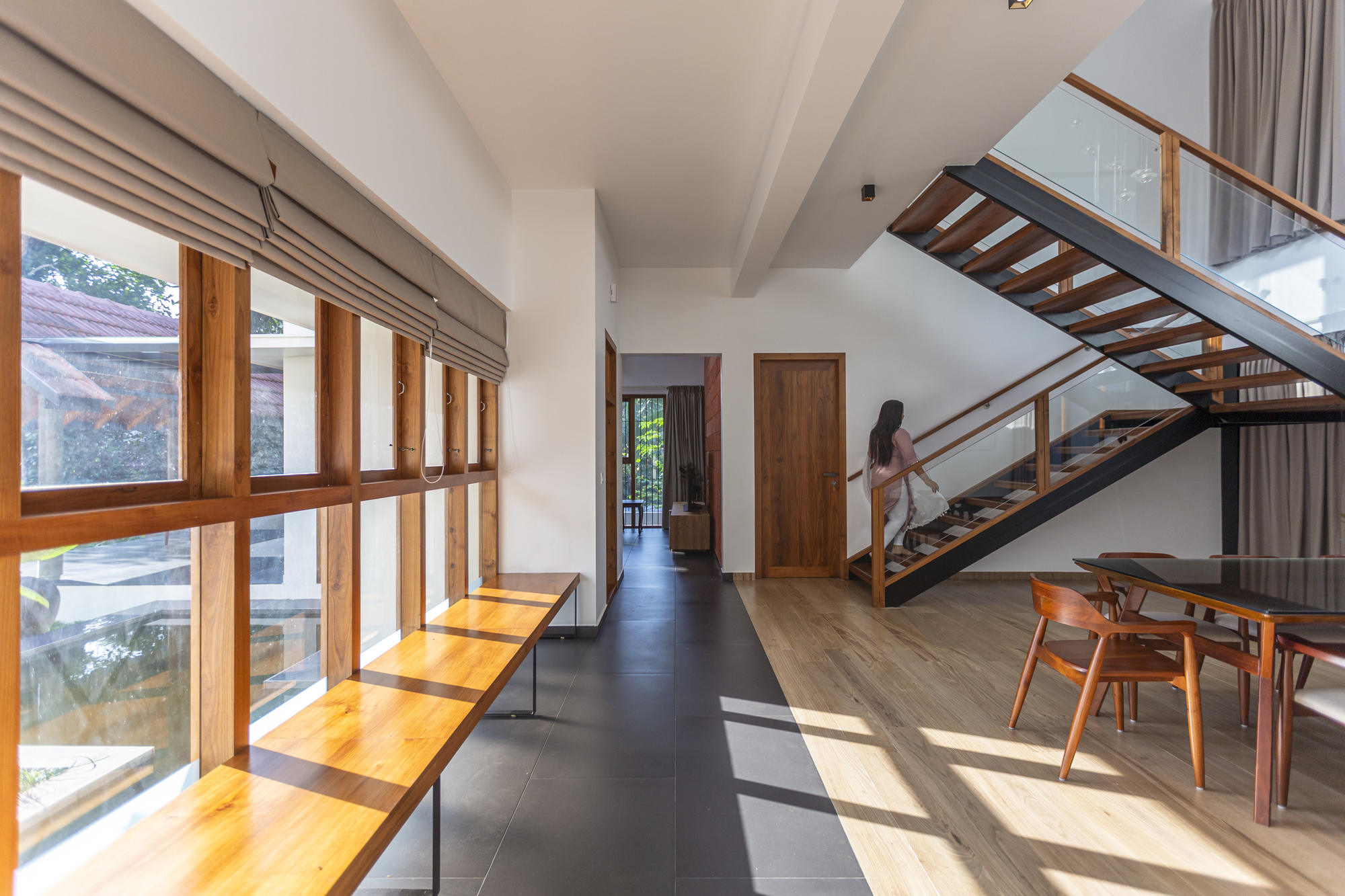 Interior hallway with open-tread timber staircase and continuous wood-framed glazing casting afternoon sunlight