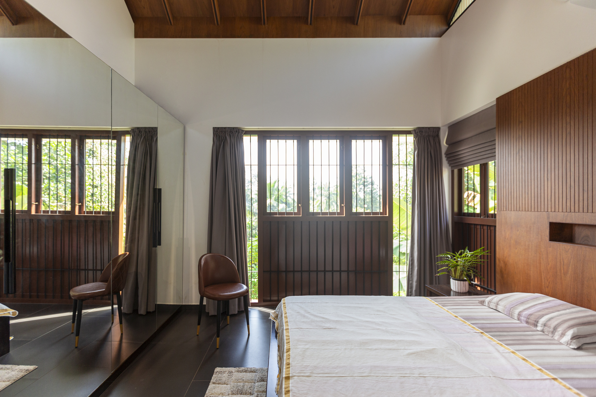 Bedroom with wood-paneled gabled ceiling and gridded windows framing the garden beyond
