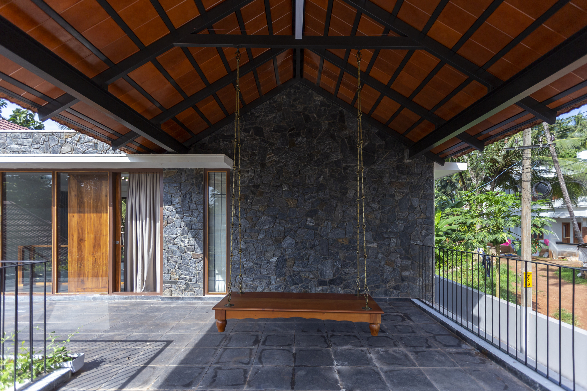 Covered terrace with exposed timber roof structure, dark stone wall and a suspended wooden swing