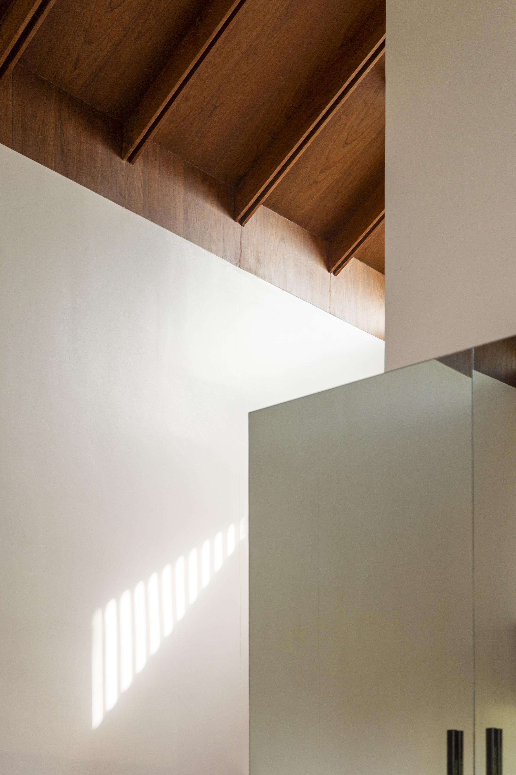 Double-height corner detail showing timber ceiling beams and sunlight patterning a white wall