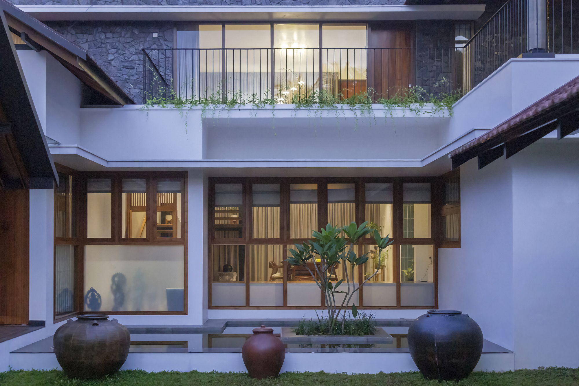 Interior courtyard view with timber-framed glazing, planted terrace above, and ceramic urns at dusk