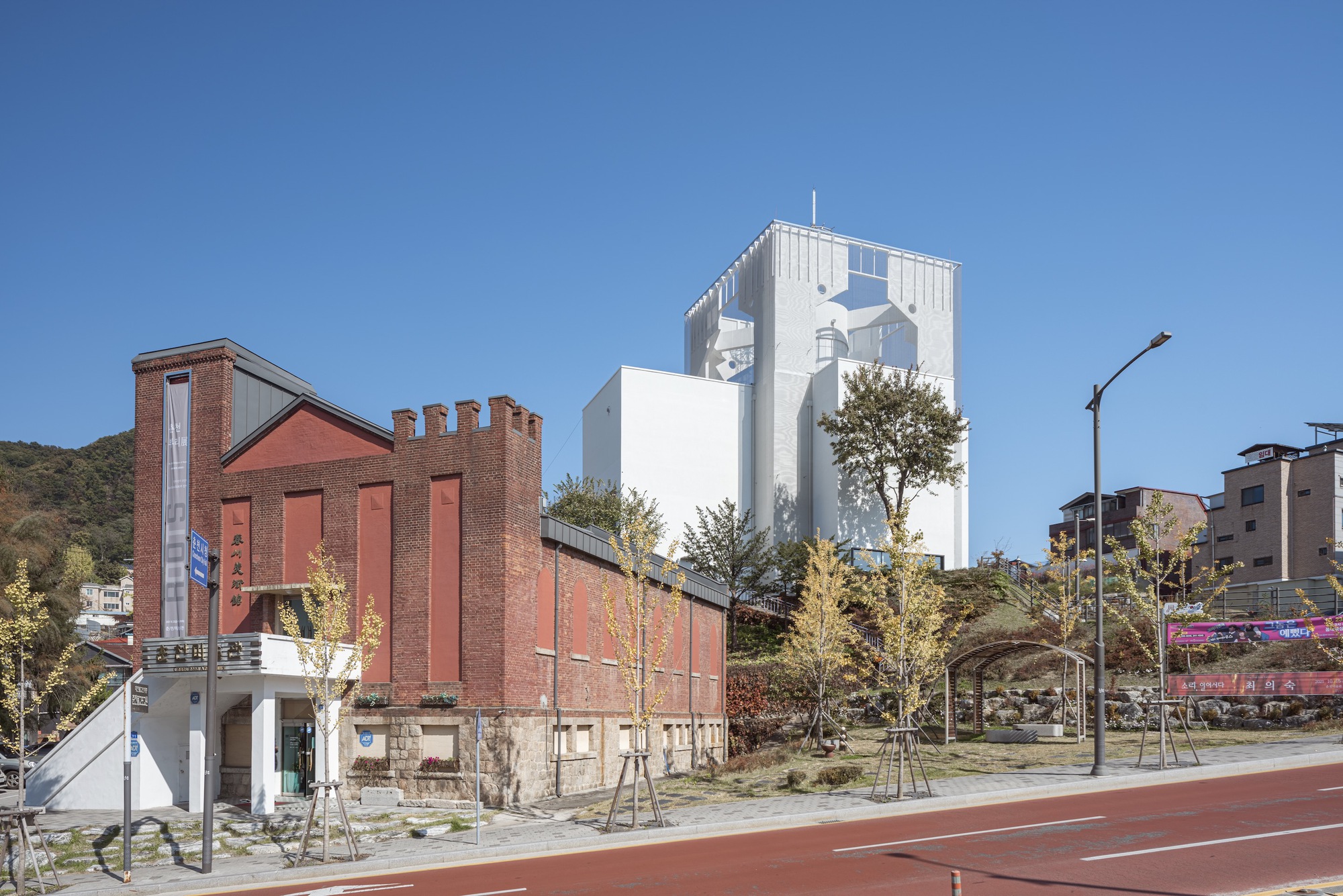 Street view of a white tower with decorative cornice rising beside a brick industrial building under clear skies