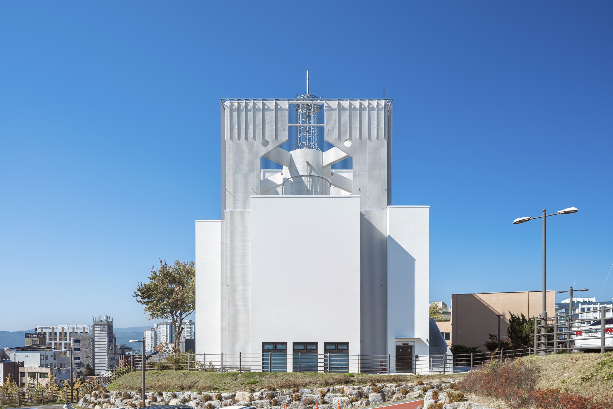 White facade with vertical corrugation and perforated upper section featuring geometric cutouts against a blue sky