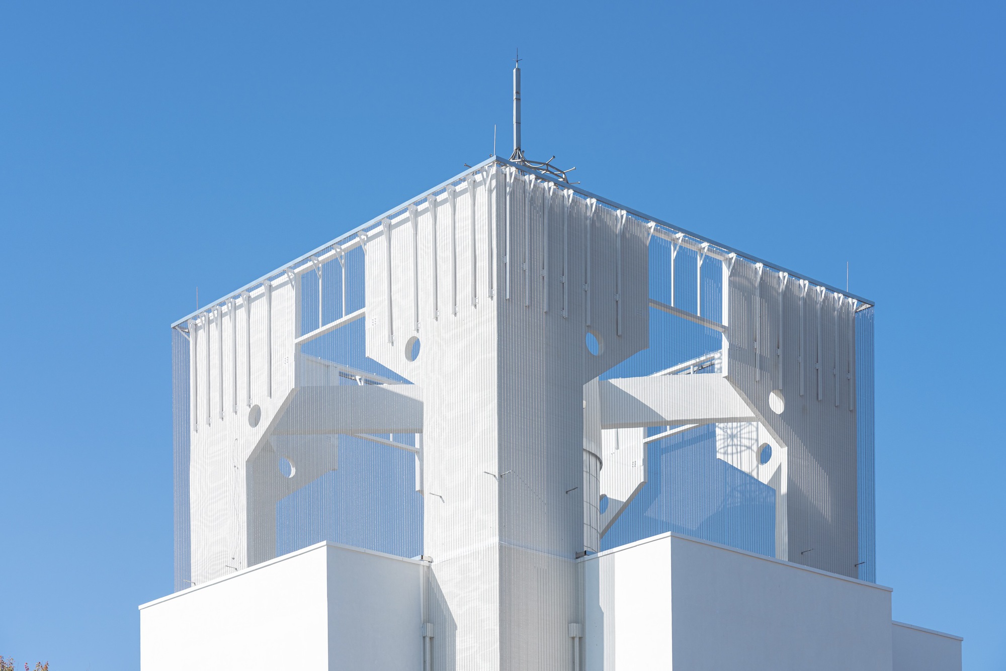 Close-up of the white corrugated tower crown with circular and geometric perforations and a central antenna