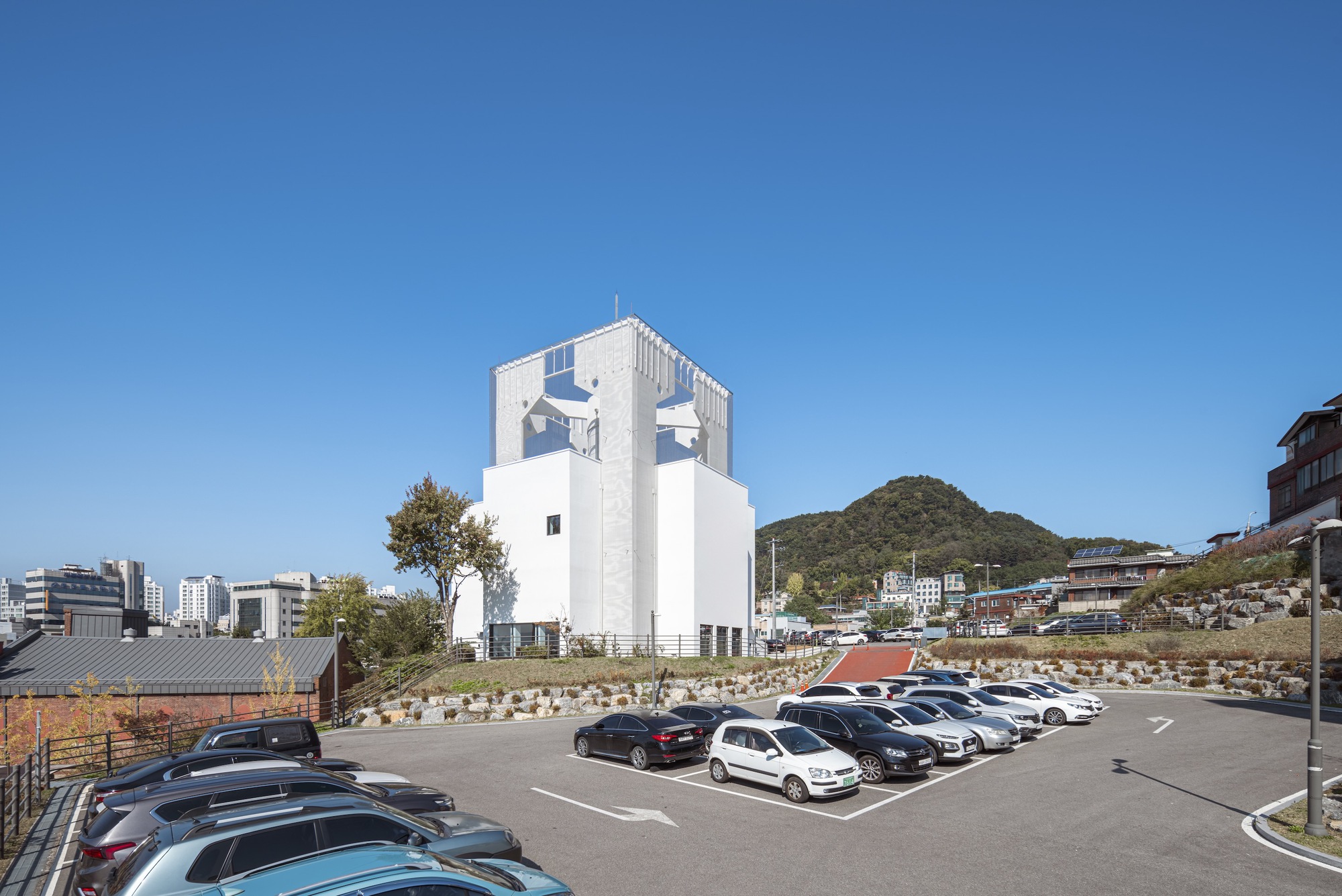 White tower standing above a parking lot with hillside and scattered trees visible in the background