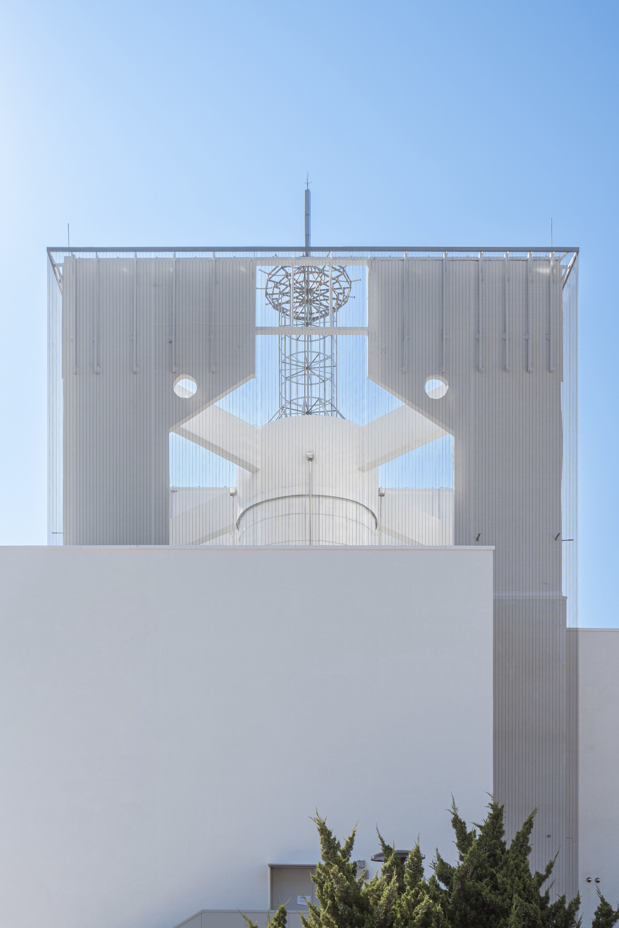 Metal screen facade with geometric cutouts framing a communications tower against clear blue sky
