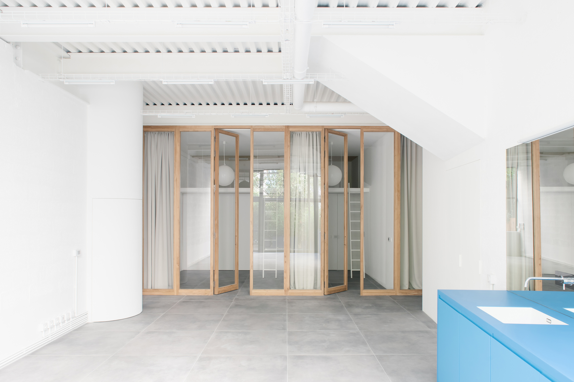Interior space with exposed timber rafters, folding timber-framed glass doors, sheer curtains and a blue kitchen counter