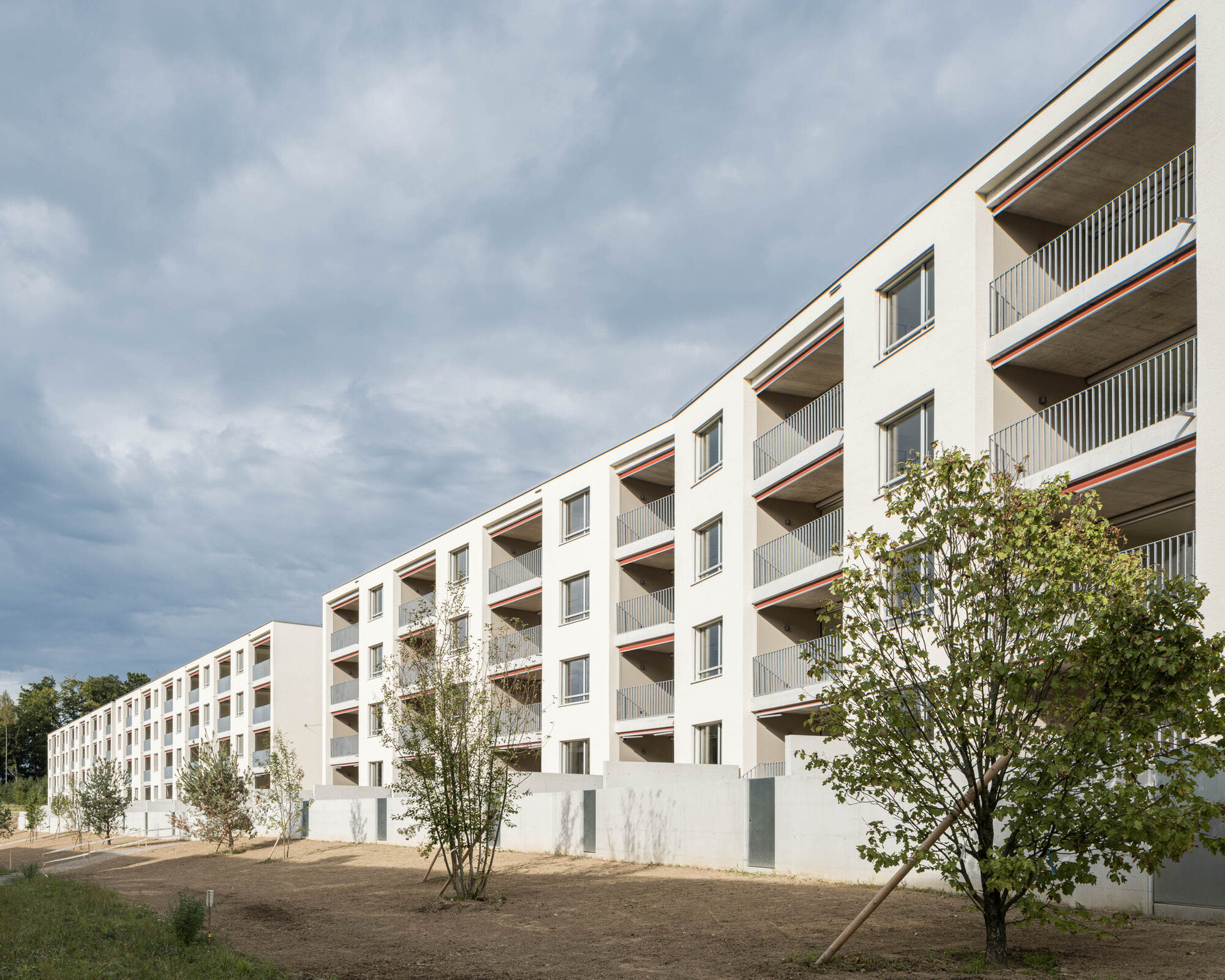 White stucco facade with recessed balconies and vertical slat railings under an overcast sky