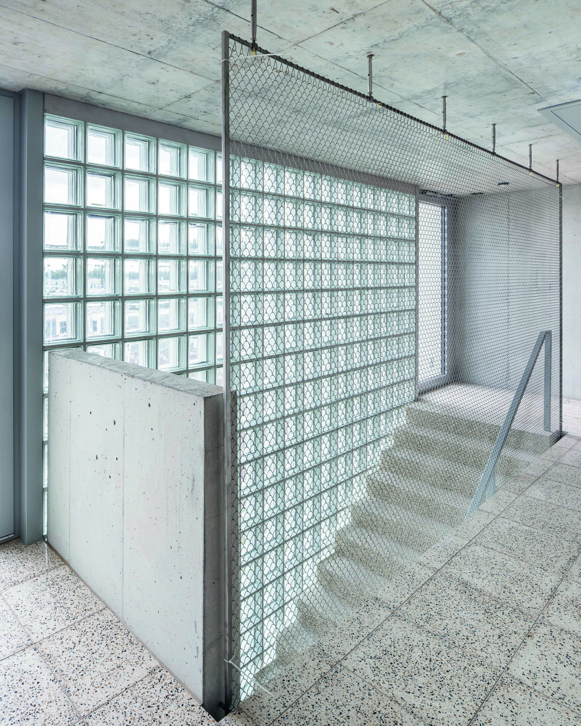 Interior corridor with patterned glass block partition and concrete balustrade beneath an exposed concrete ceiling