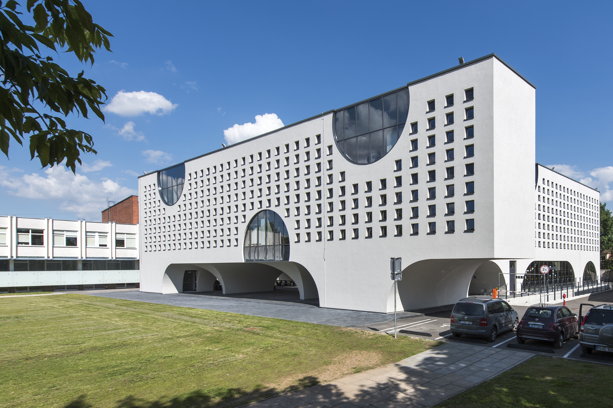 Facade with square window grid and circular glazed openings above rounded arches under a summer sky