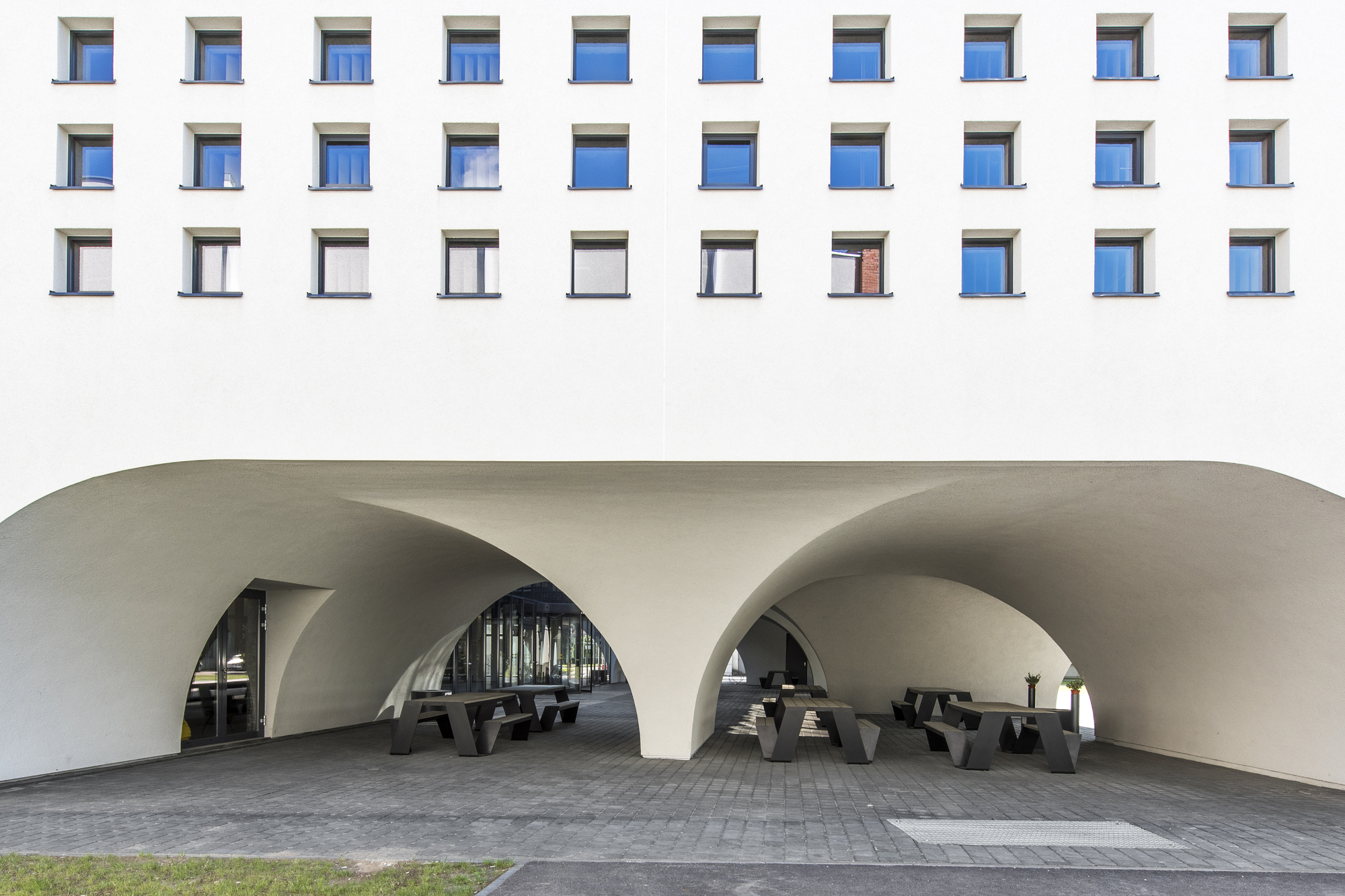 Covered entrance area with three curved archways and black timber benches on paved surface