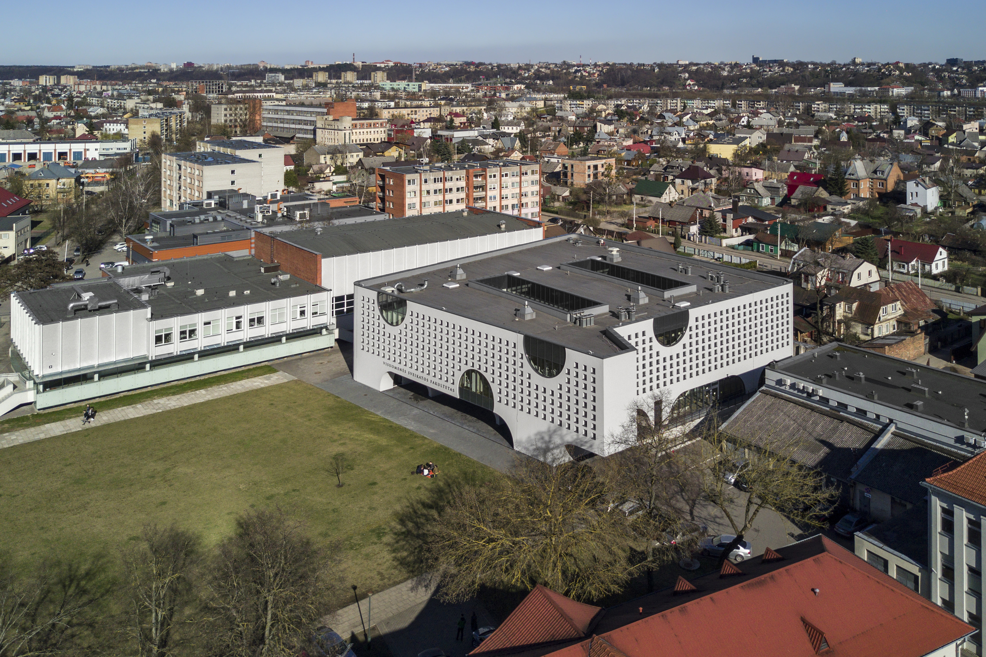 Aerial view of the U-shaped building with perforated facade and circular cutouts in a residential neighborhood