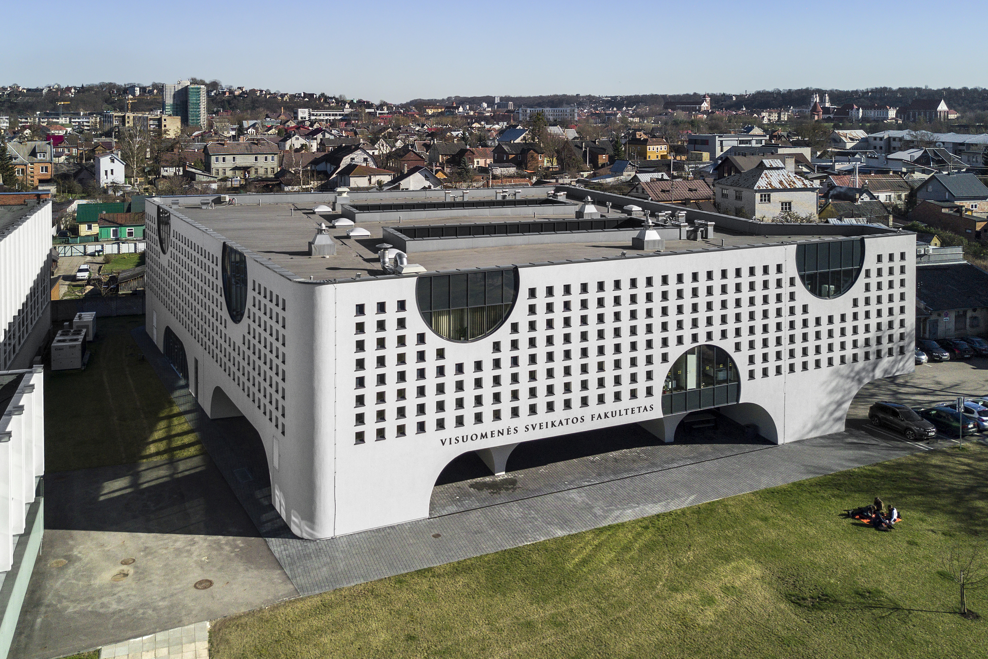 Aerial view of the white perforated facade with circular glazed cutouts and arched ground-level openings
