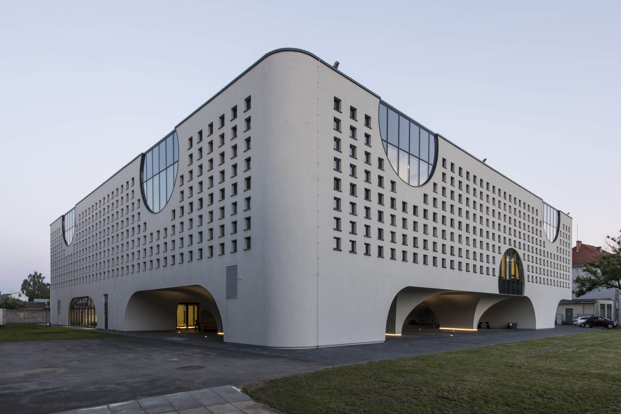 Long facade with repeating square window pattern and curved roofline under overcast evening sky