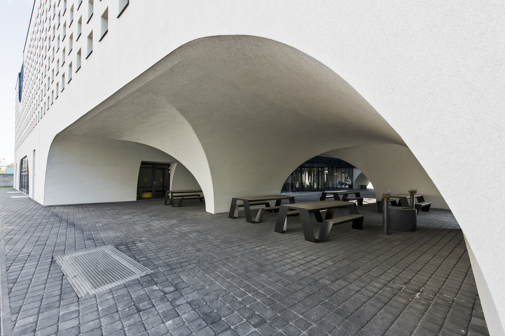 Covered terrace beneath vaulted white arches with dark timber benches on grey pavers