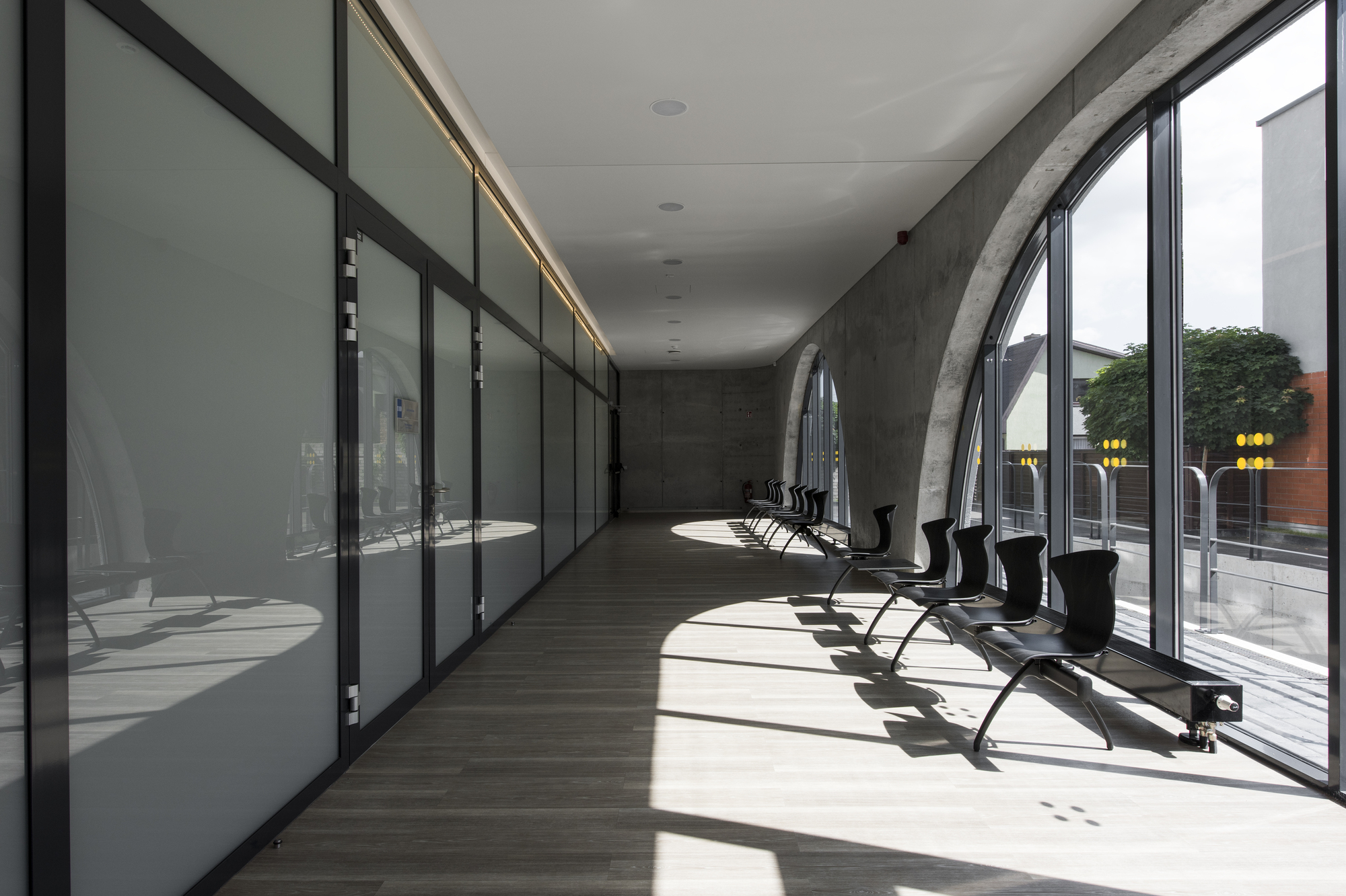 Glazed corridor with black metal frames along concrete wall and afternoon light on timber flooring