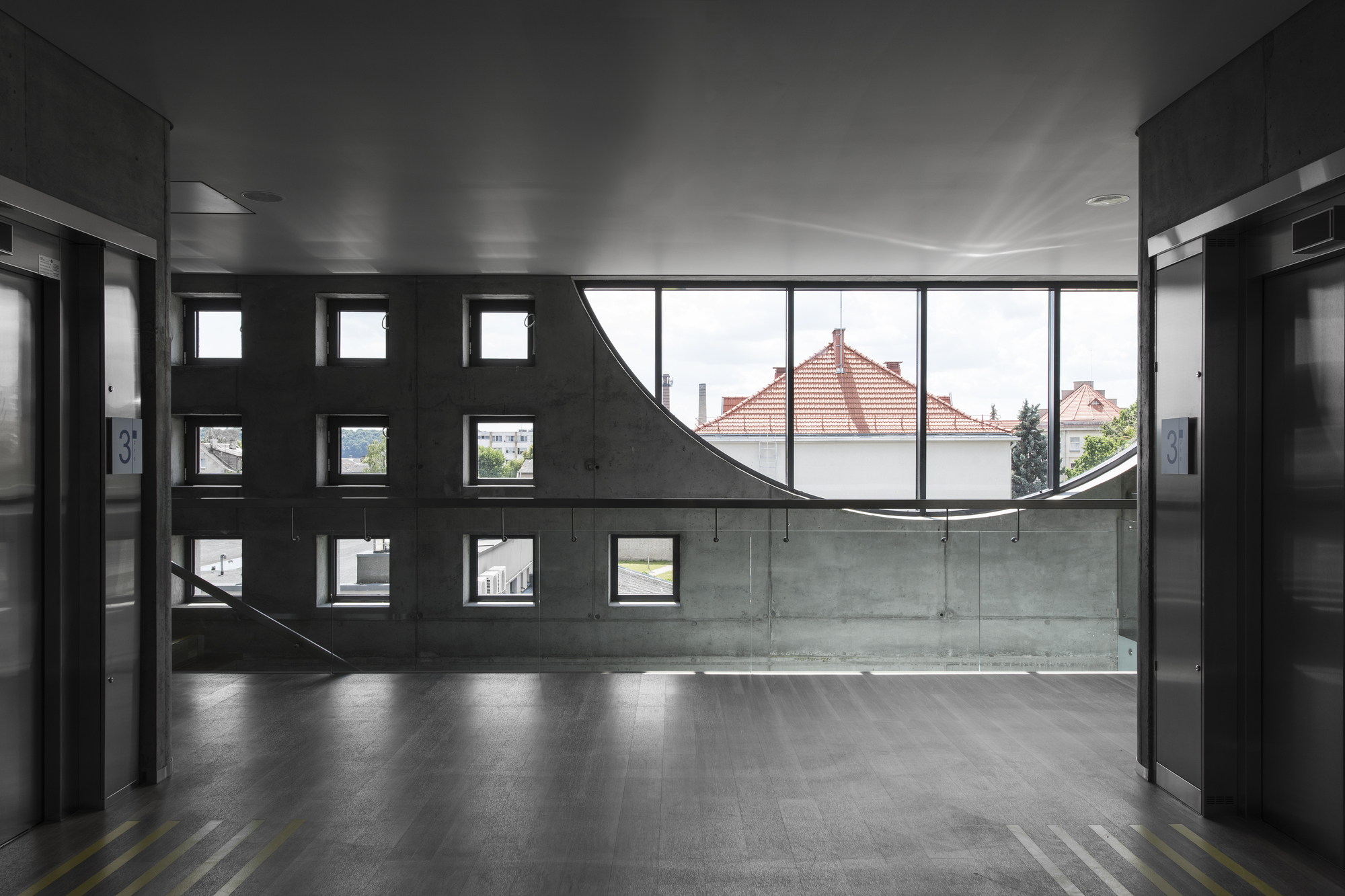 Interior lobby with curved window wall framing red tile roofs and square openings in dark concrete