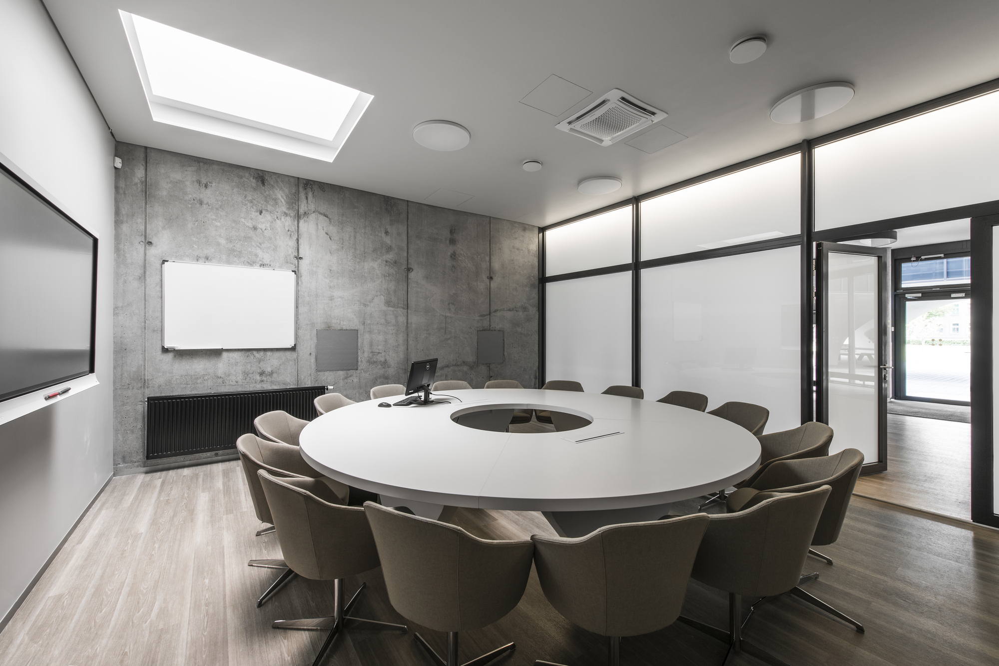Conference room with circular table beneath a skylight and exposed concrete wall with whiteboard